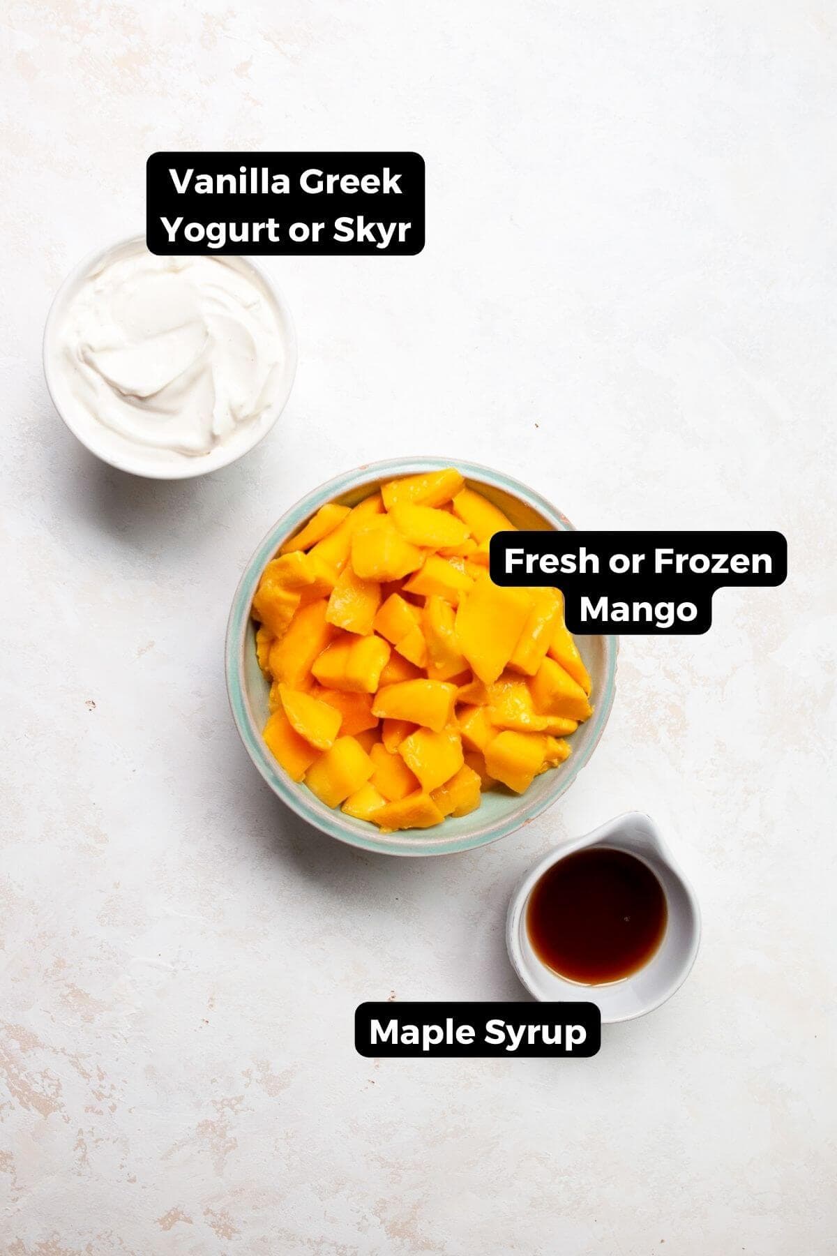 Three small bowls labeled with ingredients: fresh mango chunks, Greek yogurt, and maple syrup.