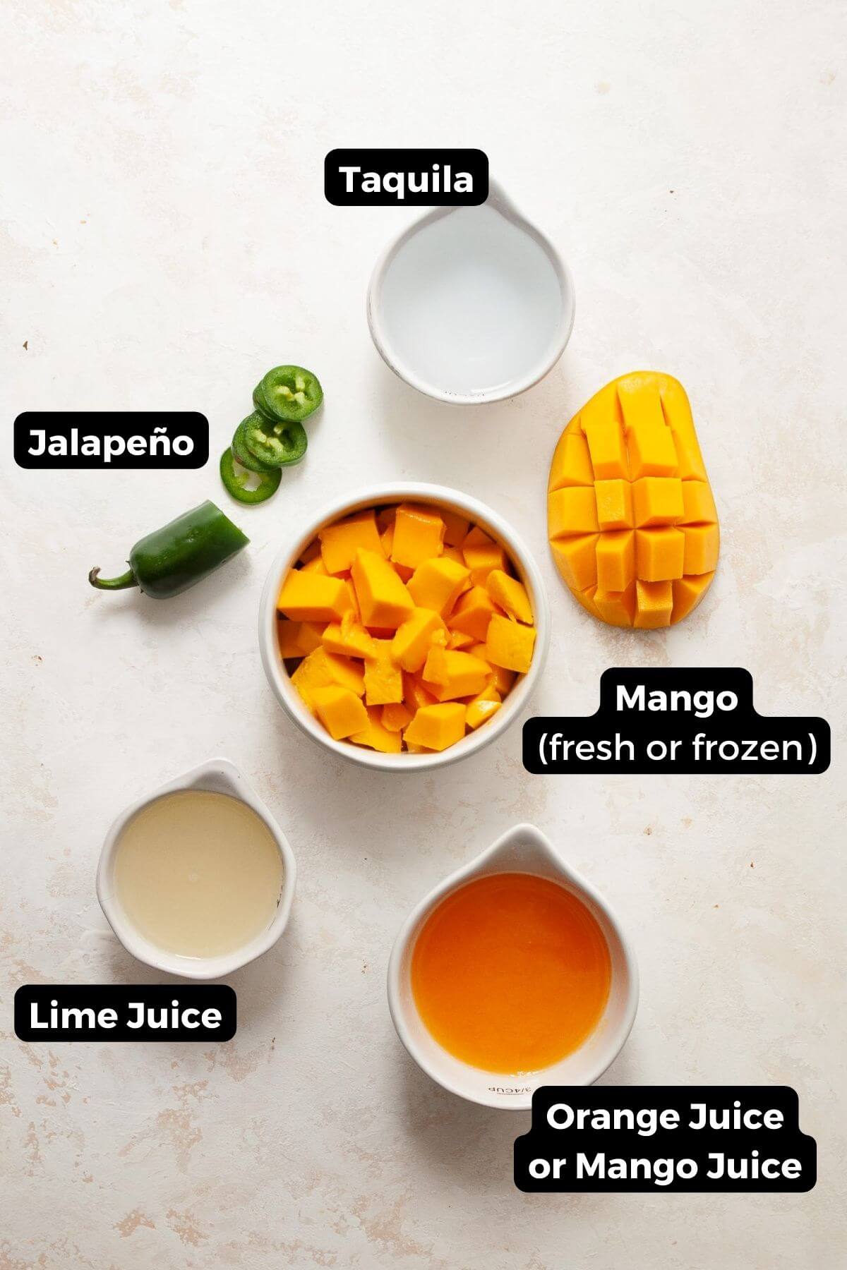 All five ingredients in small bowls with labels, including: taquila, lime juice, mango juice, mango, and jalapeño.