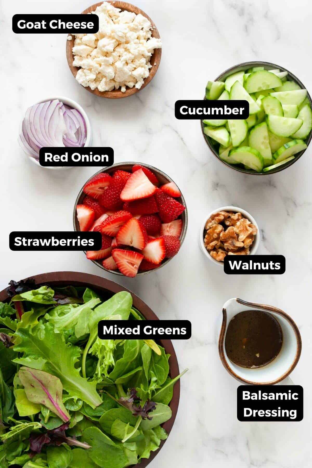 All ingredients in this strawberry goat cheese salad, including: mixed green with spinach, cucumbers, fresh strawberries, red onion, walnuts, goat cheese, and homemade balsamic dressing.