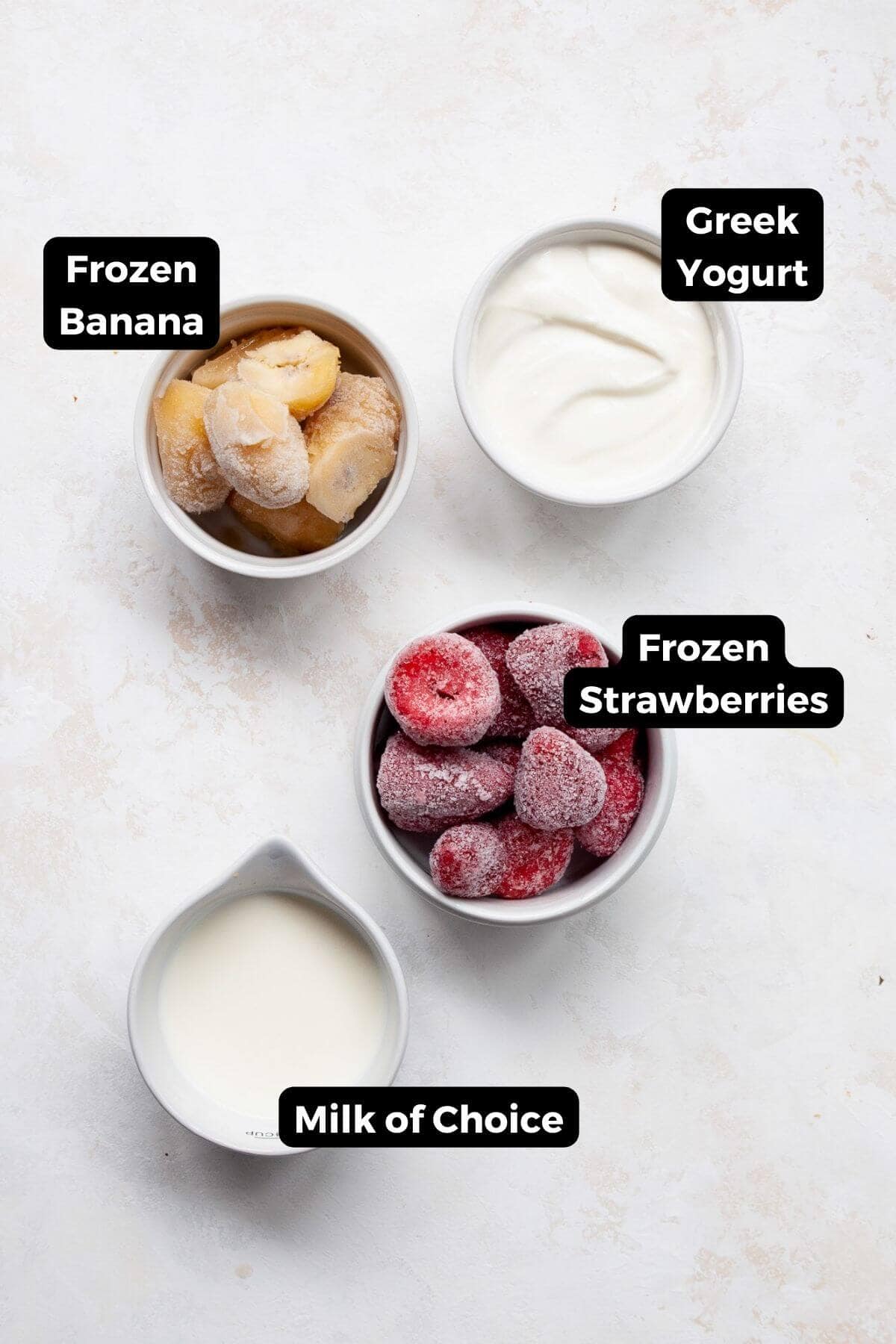 All ingredients in a strawberry smoothie bowl, including: frozen banana, Greek yogurt, frozen strawberries, and milk.