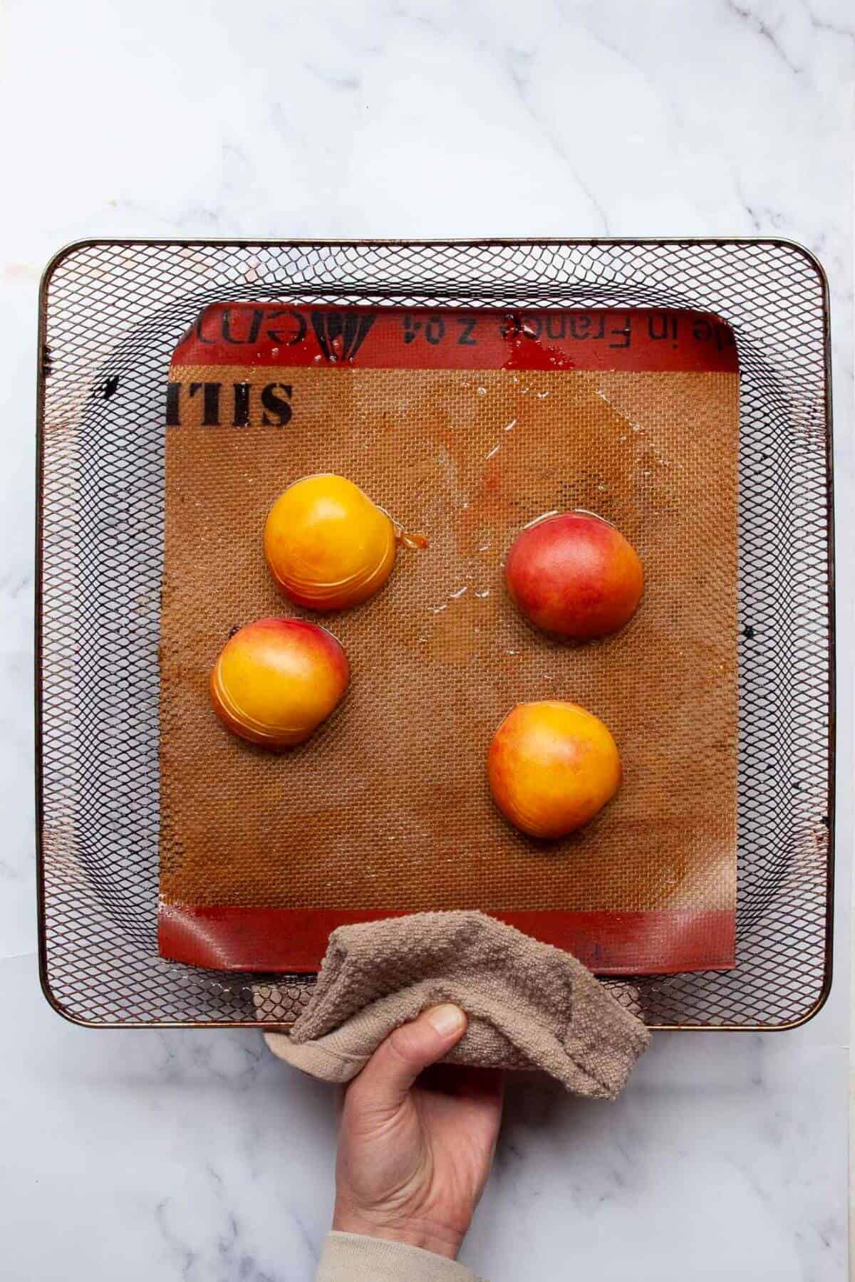 Peaches cut side down in air fryer basket before air frying.