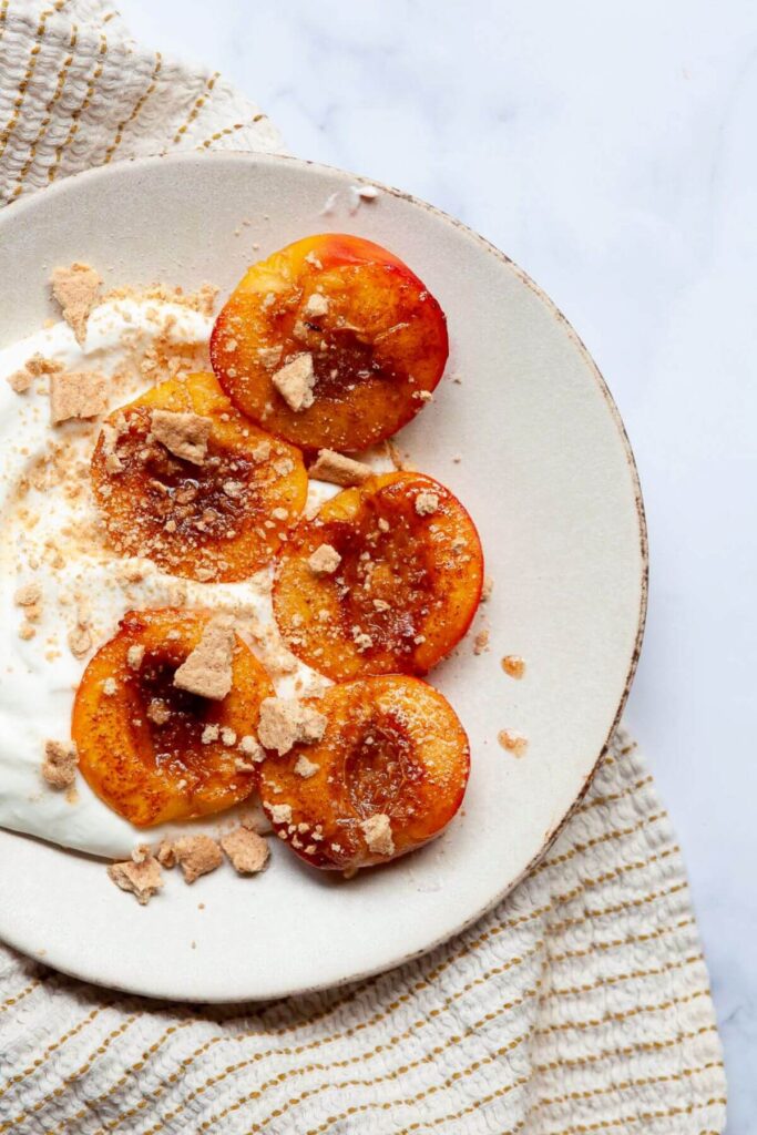 air fryer peaches on a plate with whipped cream and graham cracker crumbs