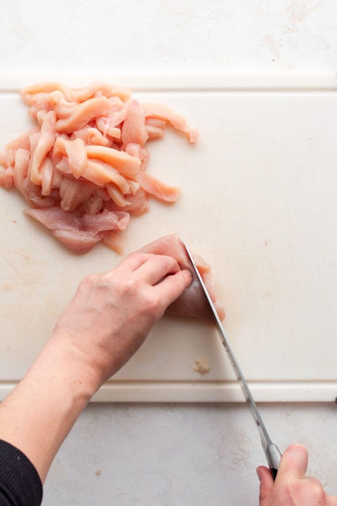 cutting raw chicken breast into thin strips