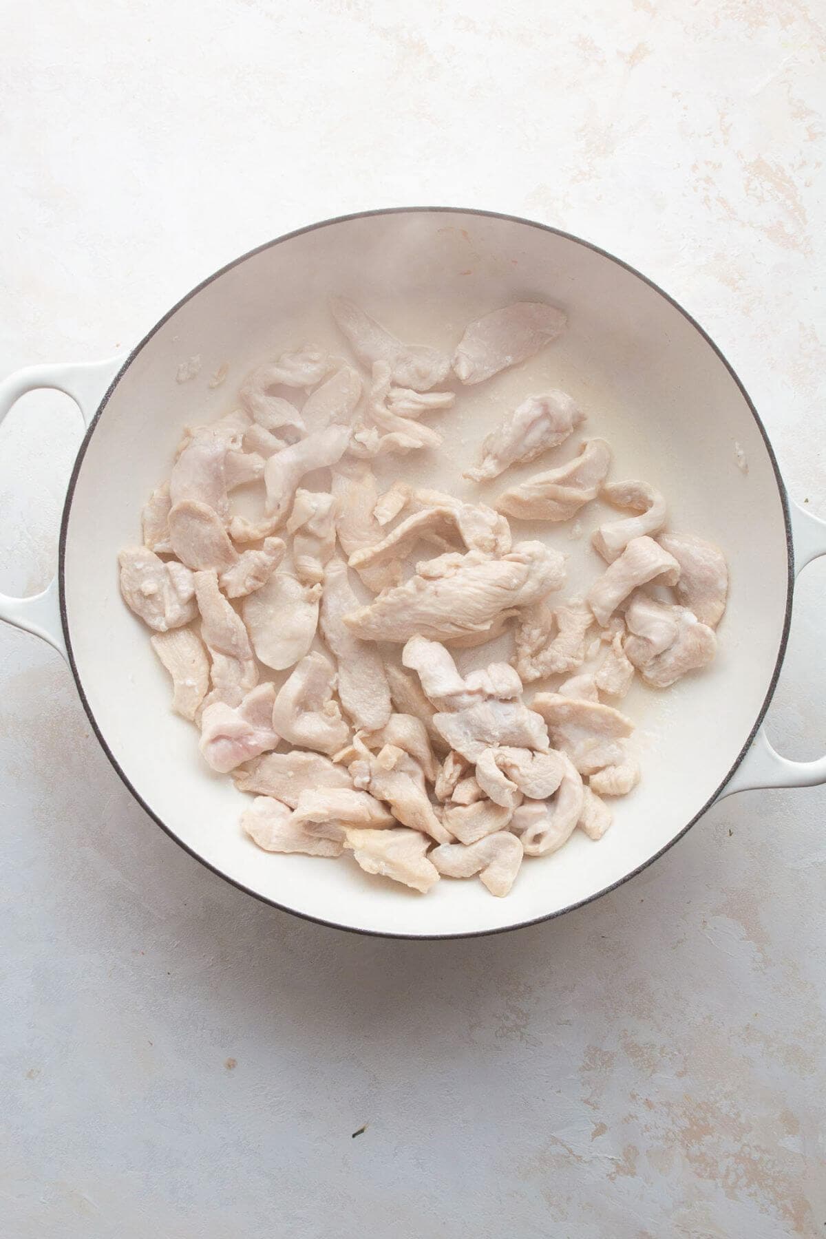 Cooking sliced chicken breast in a pan with olive oil.