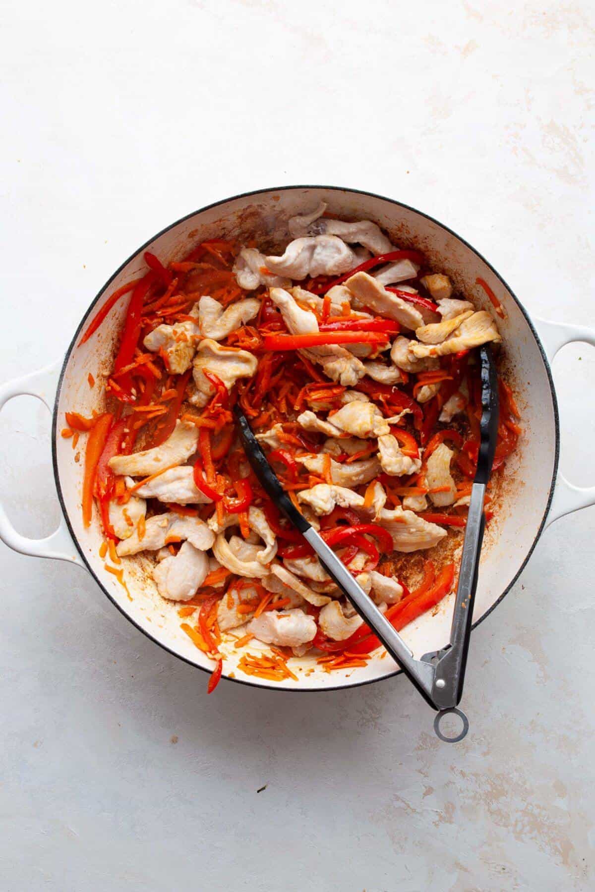 Cooked chicken added back to the pan with bell peppers and carrots.