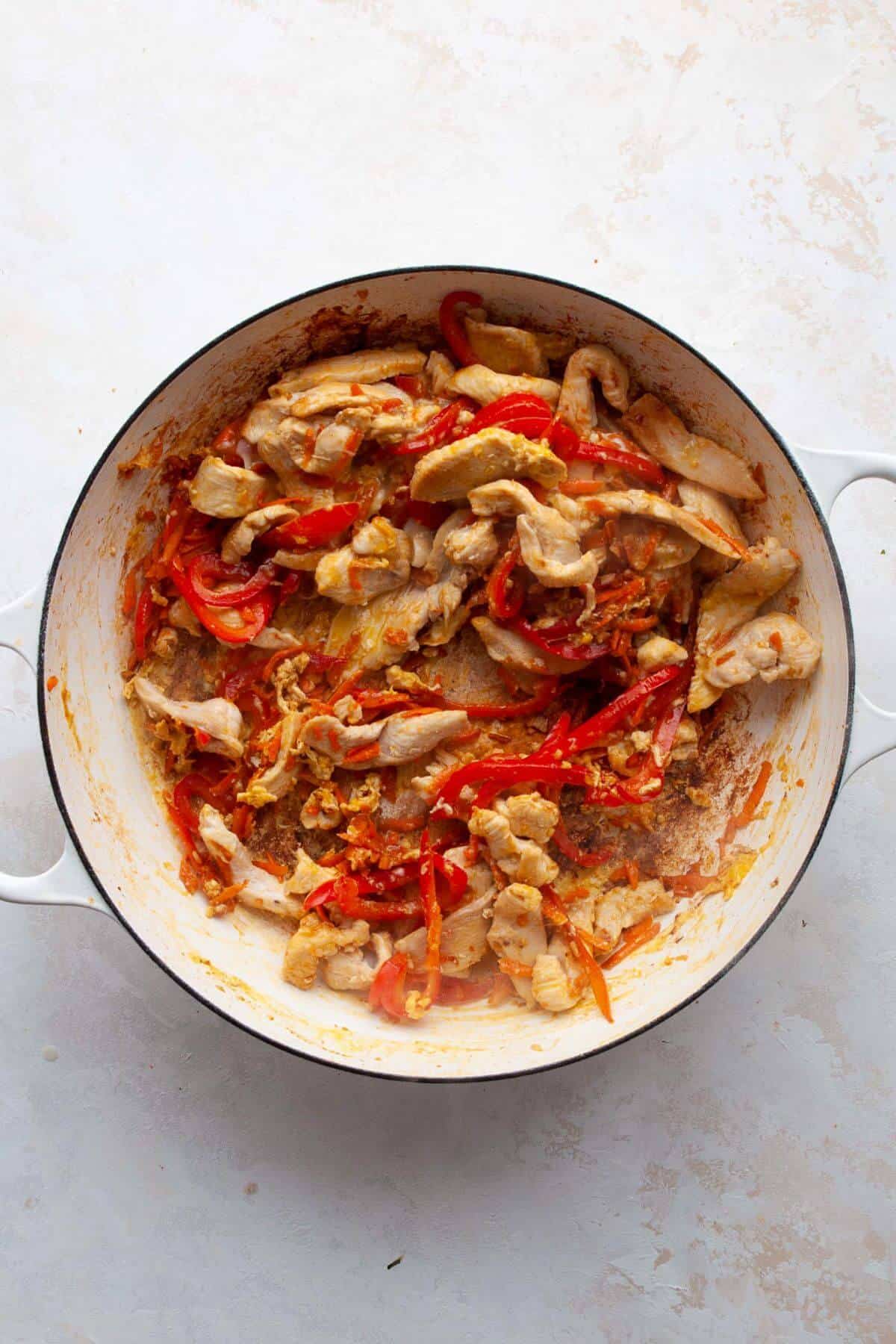Scrambling eggs in the pan with peppers, carrots, and chicken.