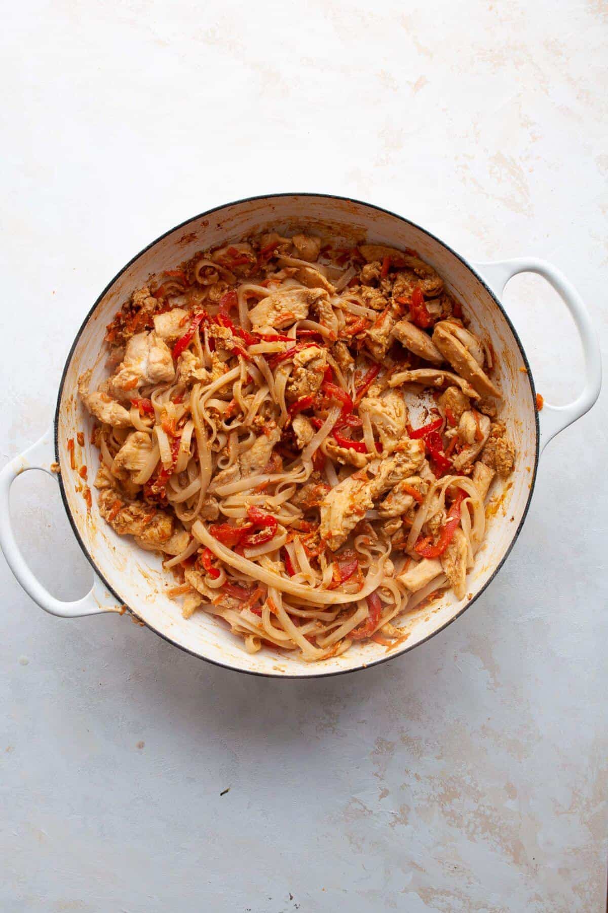Adding cooked brown rice noodles and sauce to the pan with chicken and vegetables.