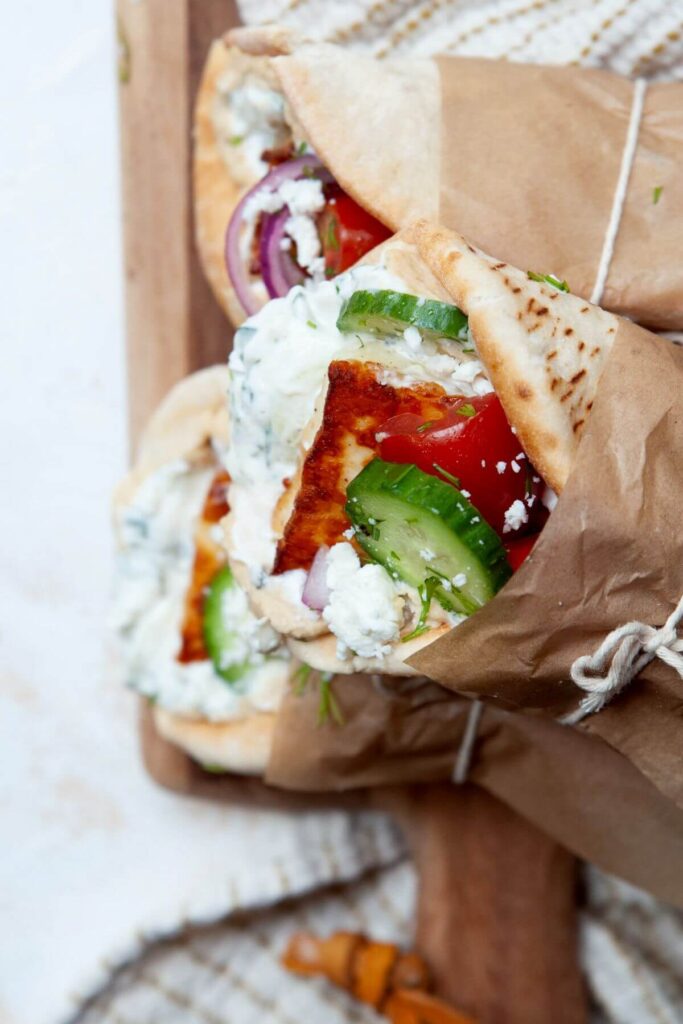 holding a Greek halloumi gyro wrapping in parchment paper