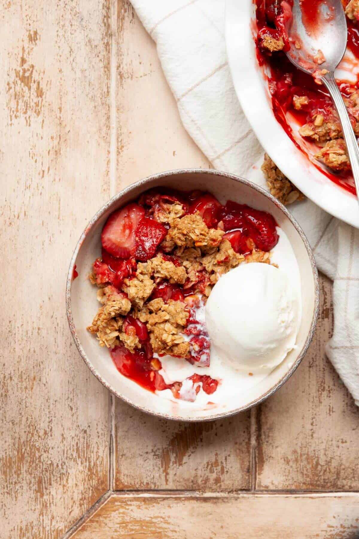 Gluten-free strawberry crumble in a bowl with vanilla ice cream.
