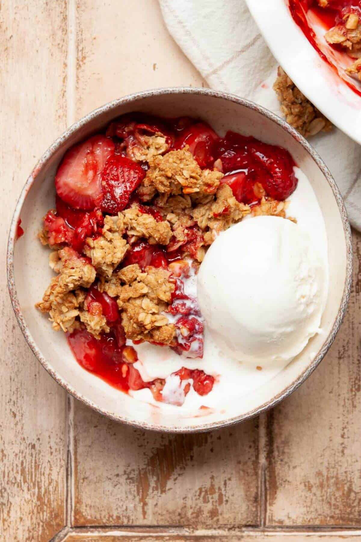 Healthy strawberry crumble served warm in a bowl with a scoop of vanilla ice cream melting on top.
