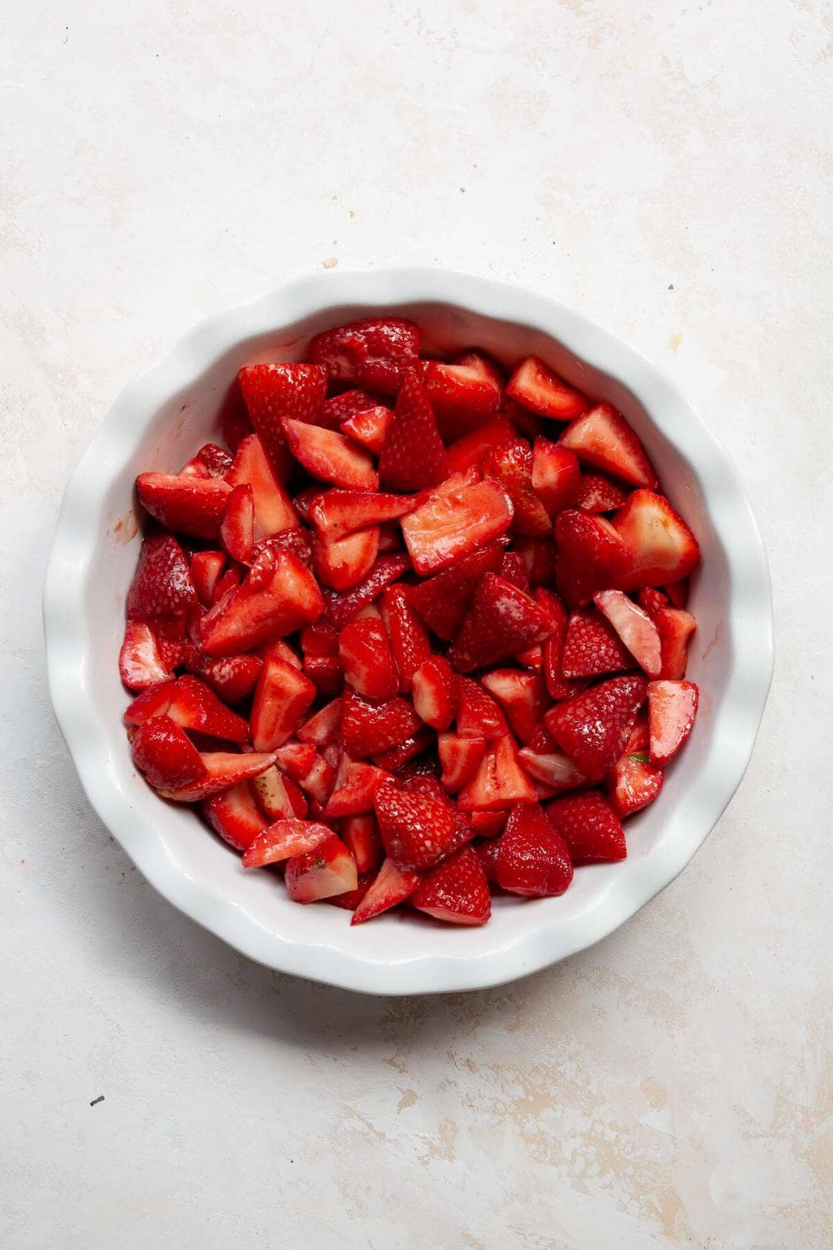 Sliced strawberries spread in a greased pie dish before being topped with oat crumble.