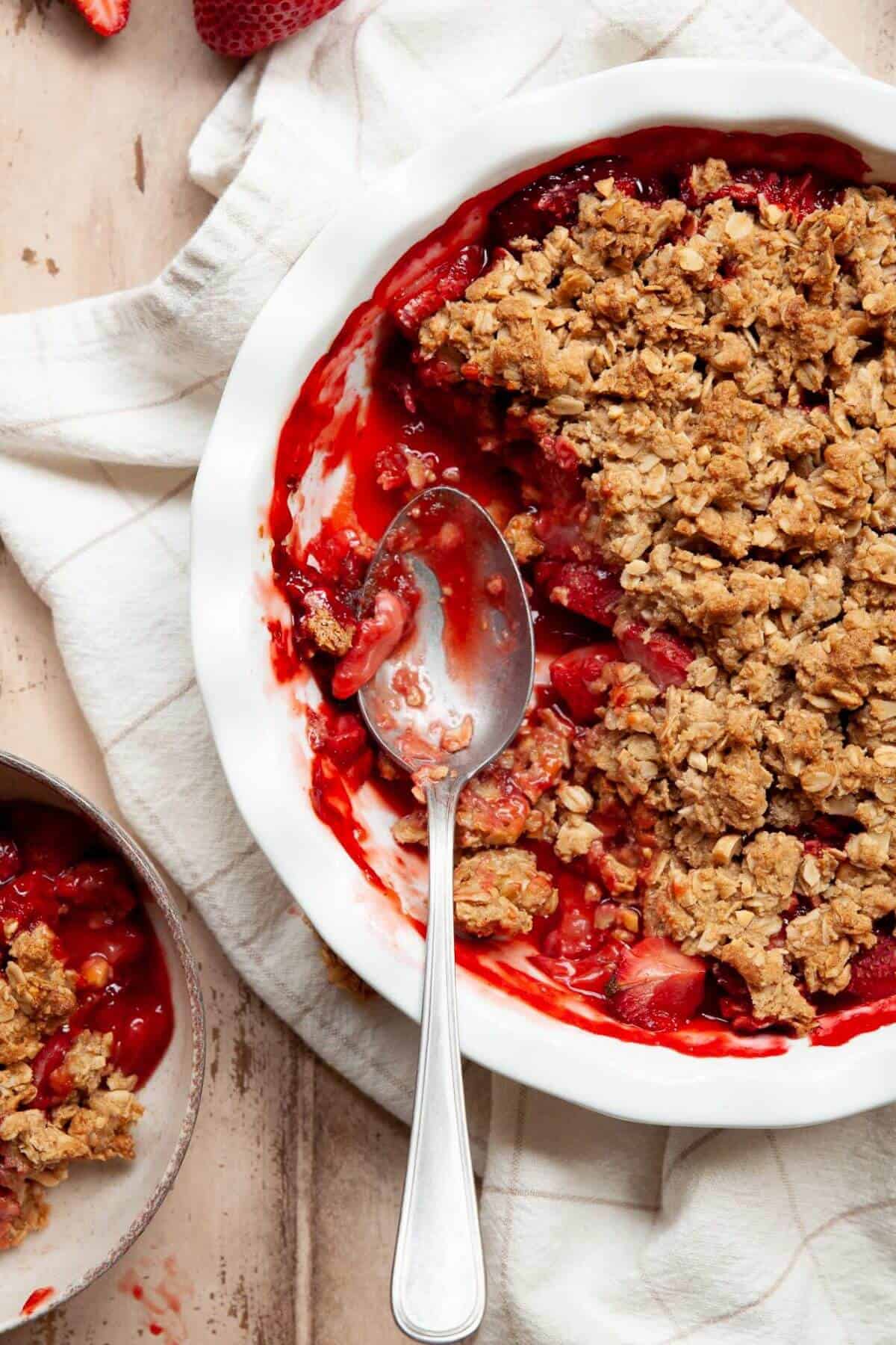 Spoon scooping into a warm strawberry crumble showing the jammy filling and crisp oat topping.