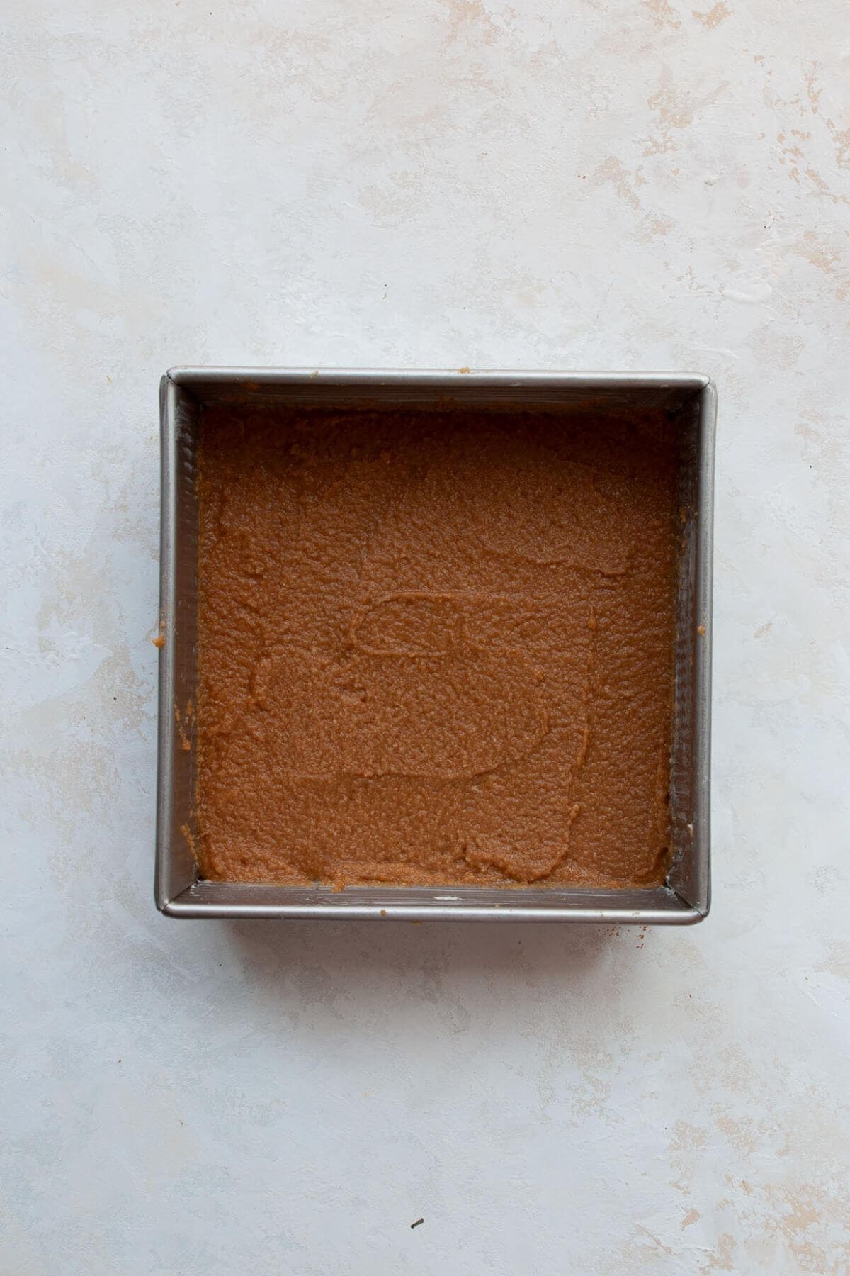 Half of coffee cake batter spread into a lined square baking pan.
