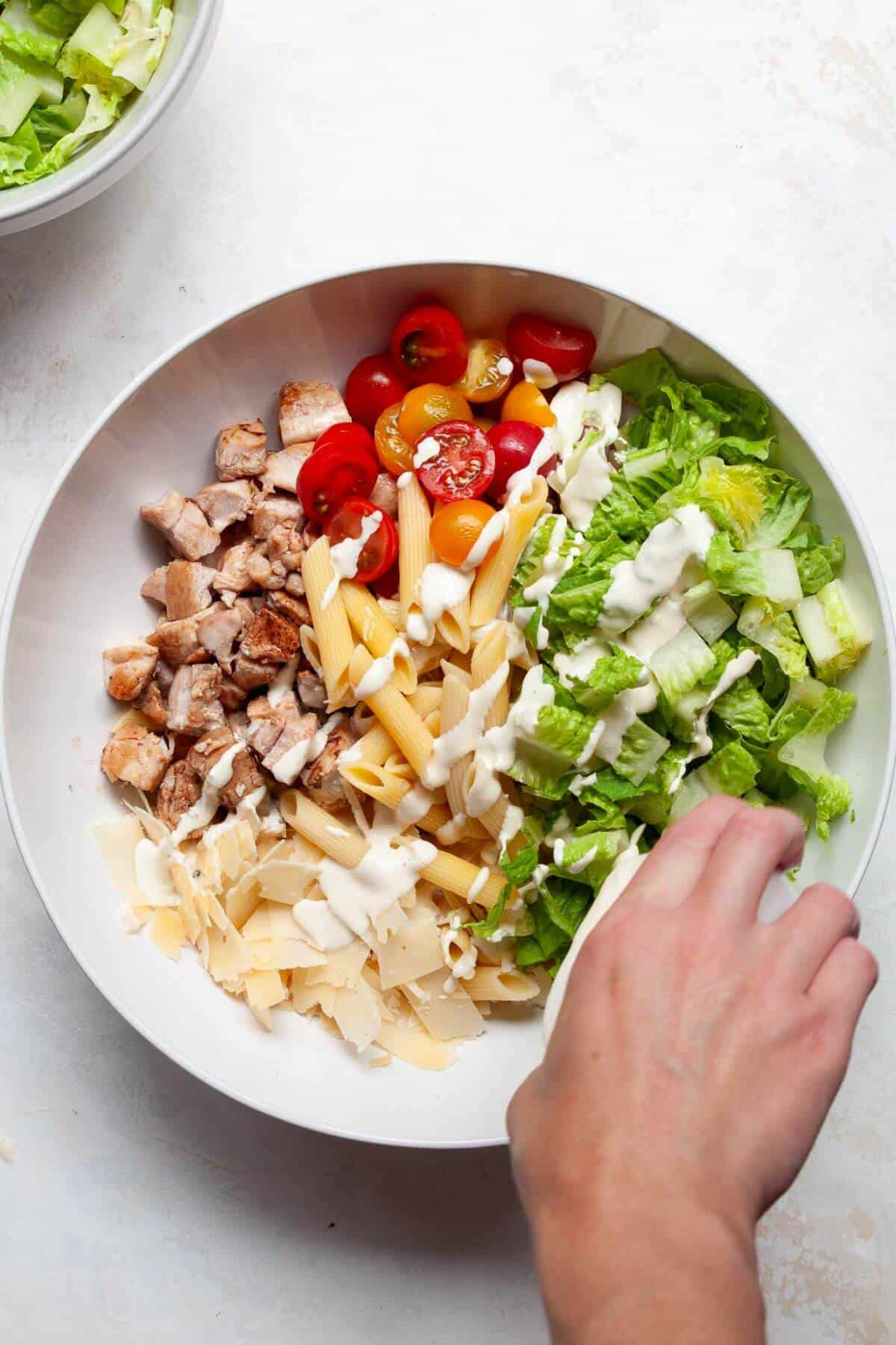 pouring healthy caesar dressing on top of pasta salad in a bowl