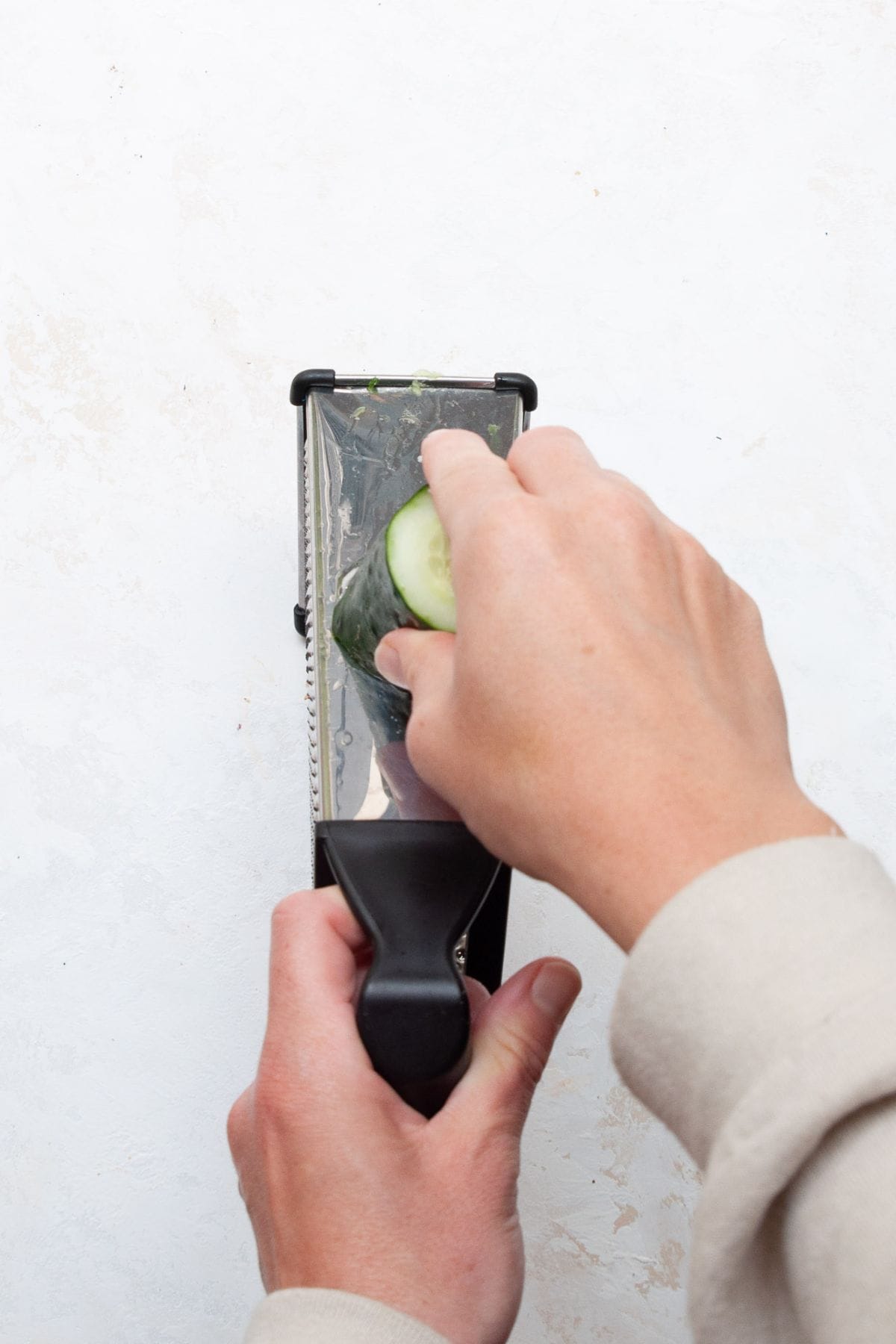 thinly slicing a cucumber on a box grater