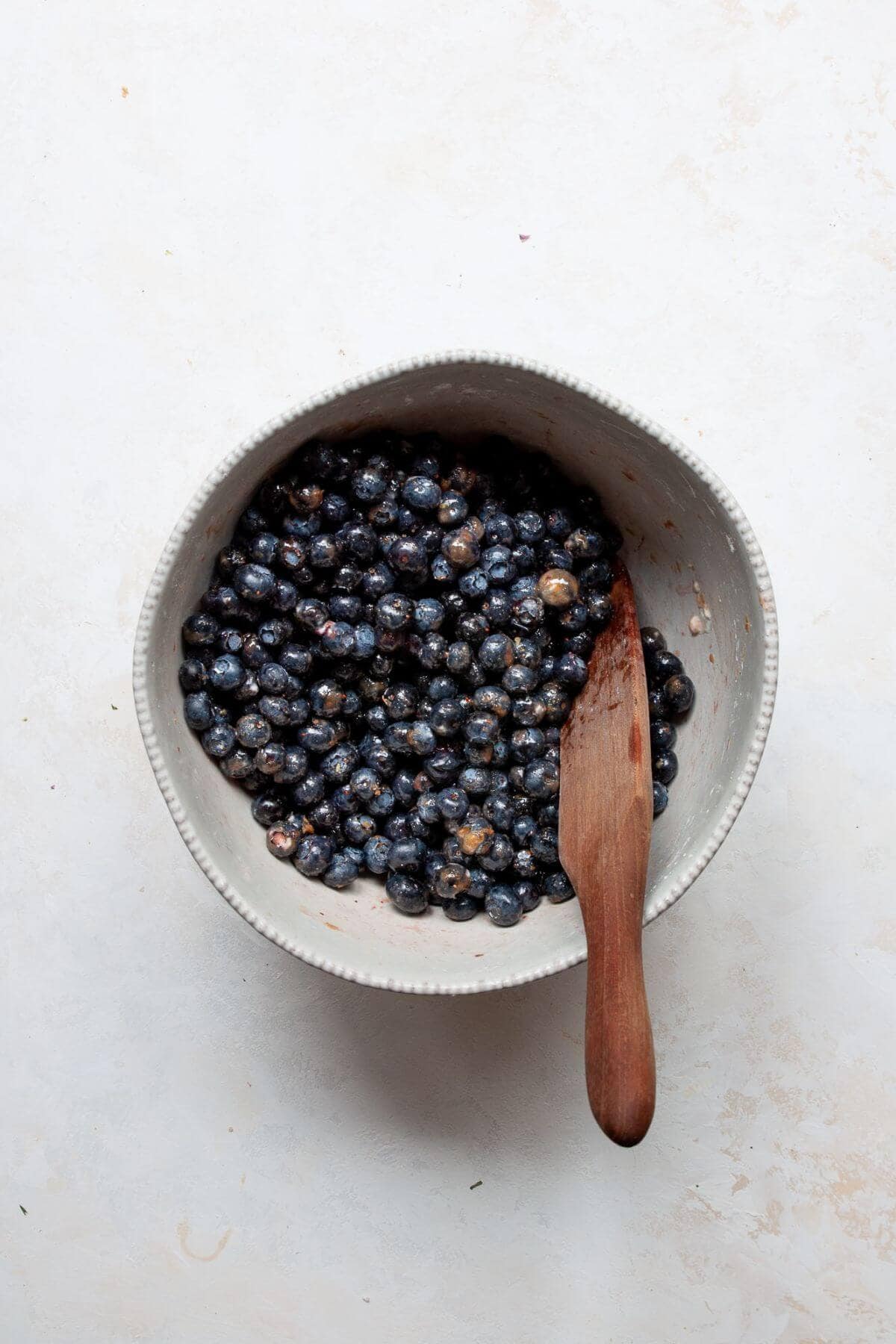 Fresh blueberries being tossed with coconut sugar, lemon juice, and cornstarch in a white bowl.