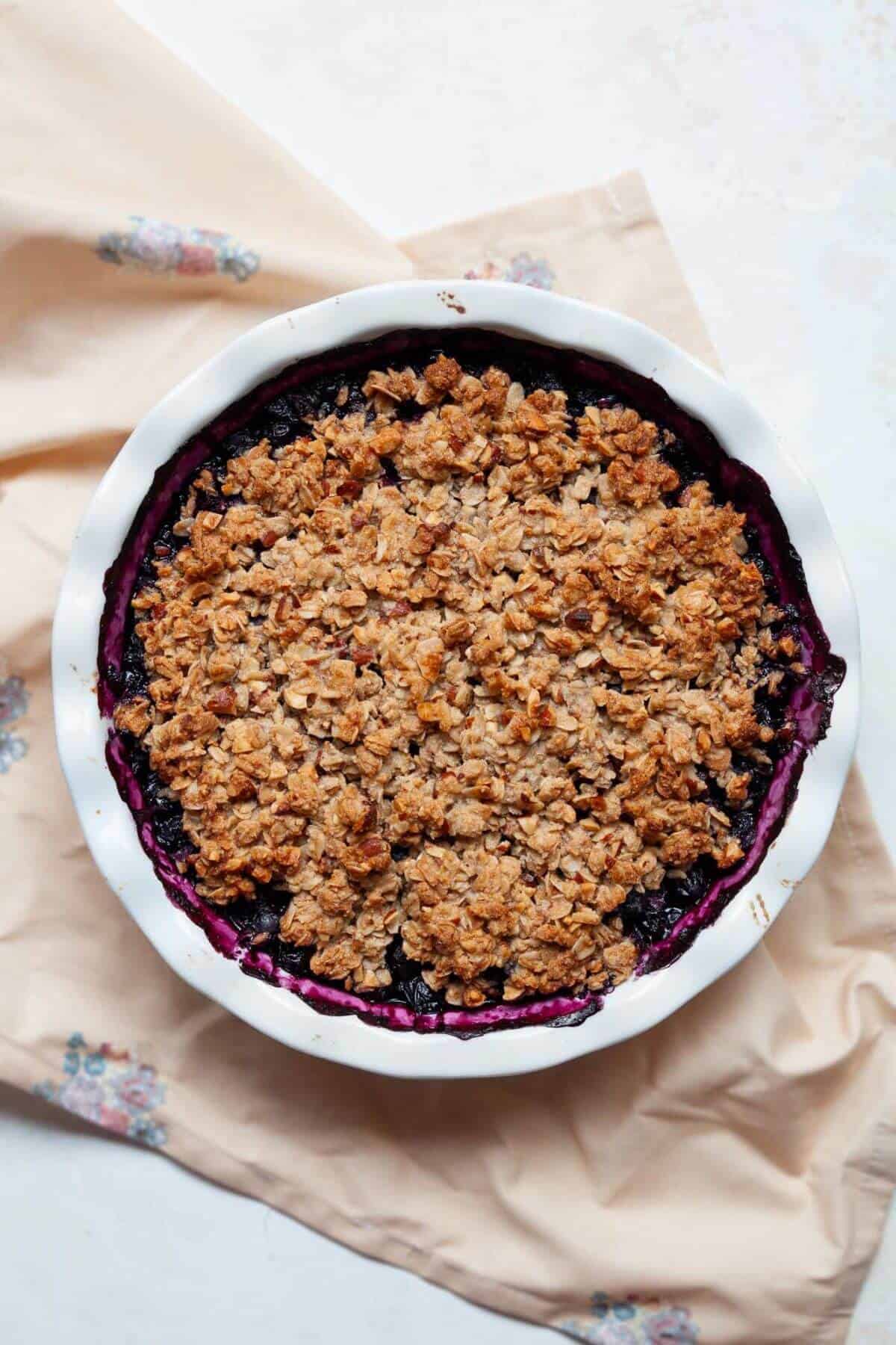 Freshly baked gluten-free blueberry crisp with a golden almond-oat crumble topping in a white round baking dish.