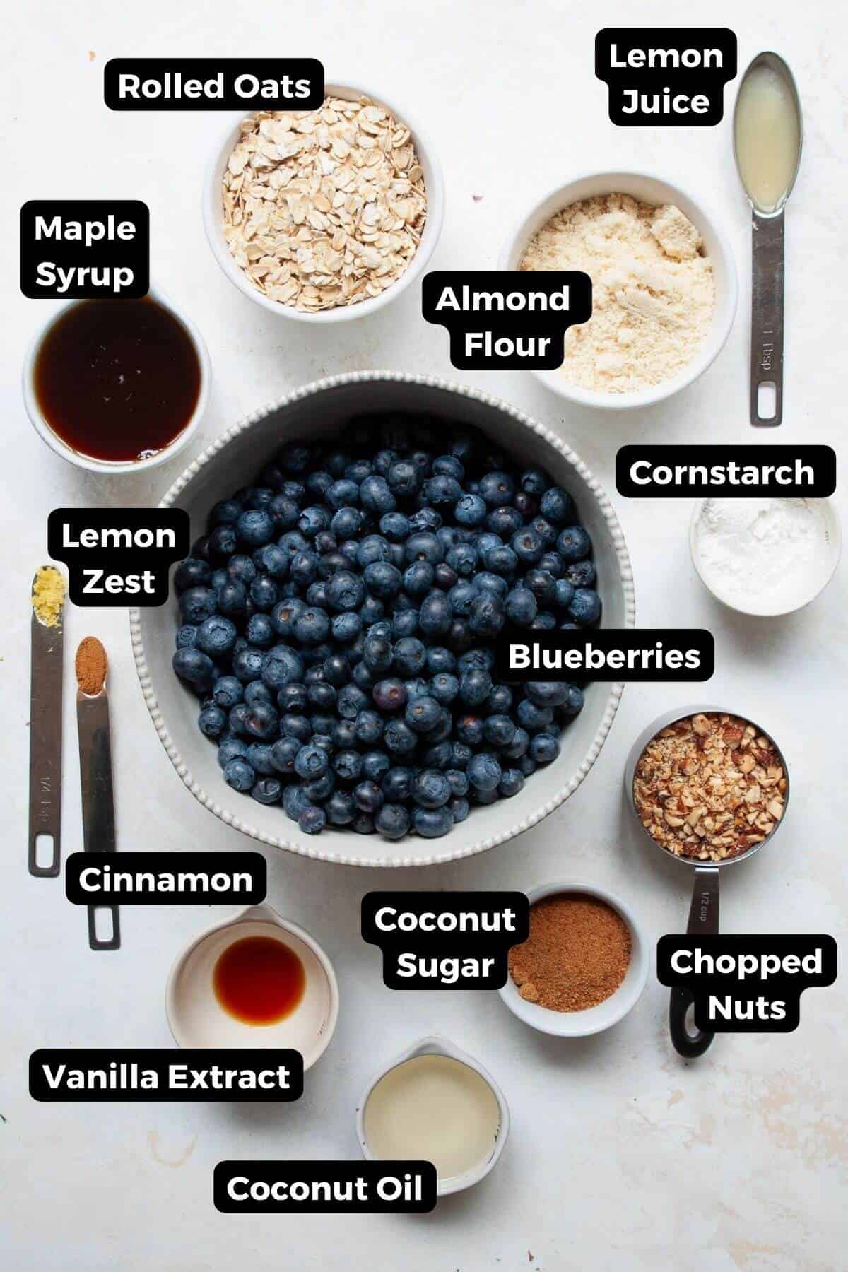 Gluten-free blueberry crisp ingredients labeled: blueberries, rolled oats, almond flour, maple syrup, coconut oil, coconut sugar, cornstarch, lemon zest, cinnamon, vanilla extract, and chopped nuts.