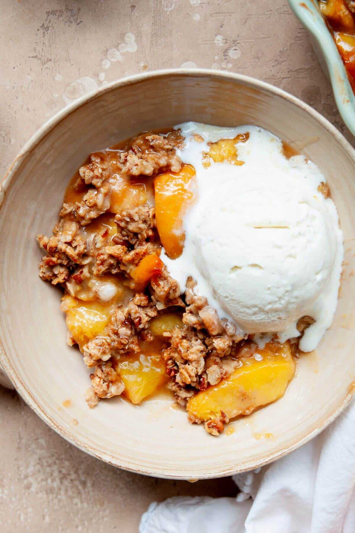 Healthy, gluten-free peach crisp served with vanilla ice cream on top.