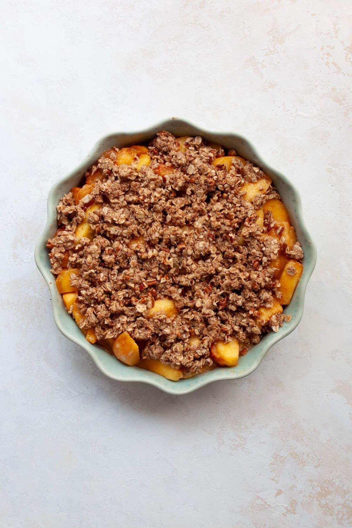 Peach filling in a pie dish topped with oat crumble before baking.