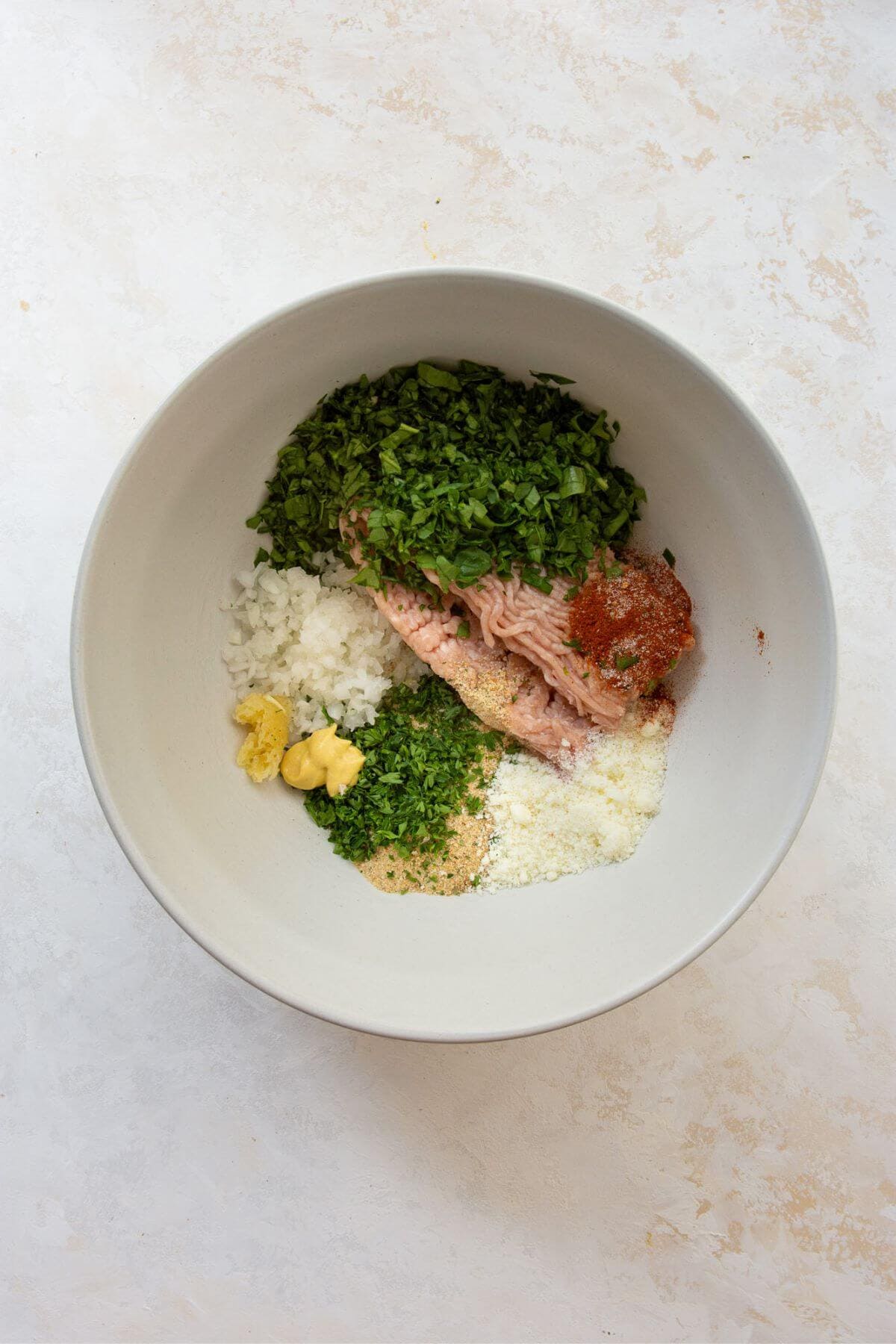 All ingredients for air fryer chicken meatballs in a large mixing bowl, including ground chicken, shredded onion, breadcrumbs, egg, parmesan, spinach, garlic, and seasonings.