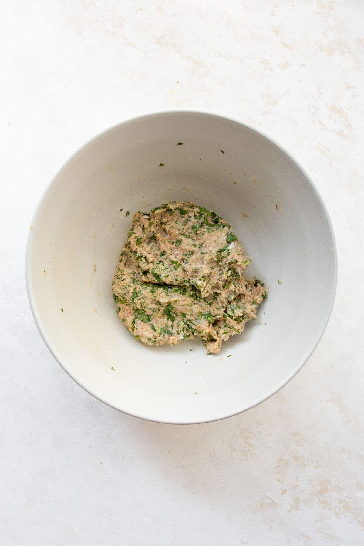 Raw chicken meatball mixture in a mixing bowl with ground chicken, spinach, breadcrumbs, egg, parmesan, garlic, onion, and seasonings combined.