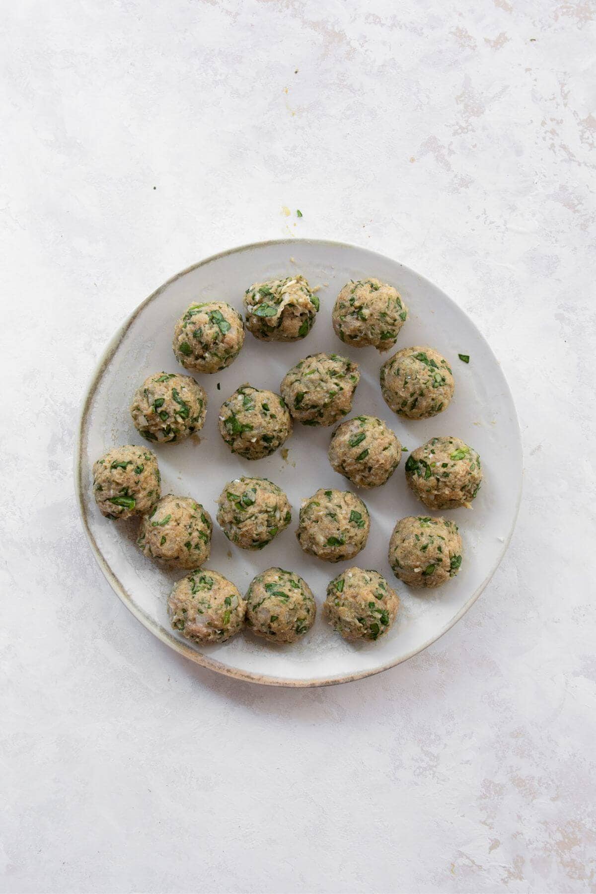 Uncooked chicken meatballs rolled and arranged on a plate, ready to be air fried.