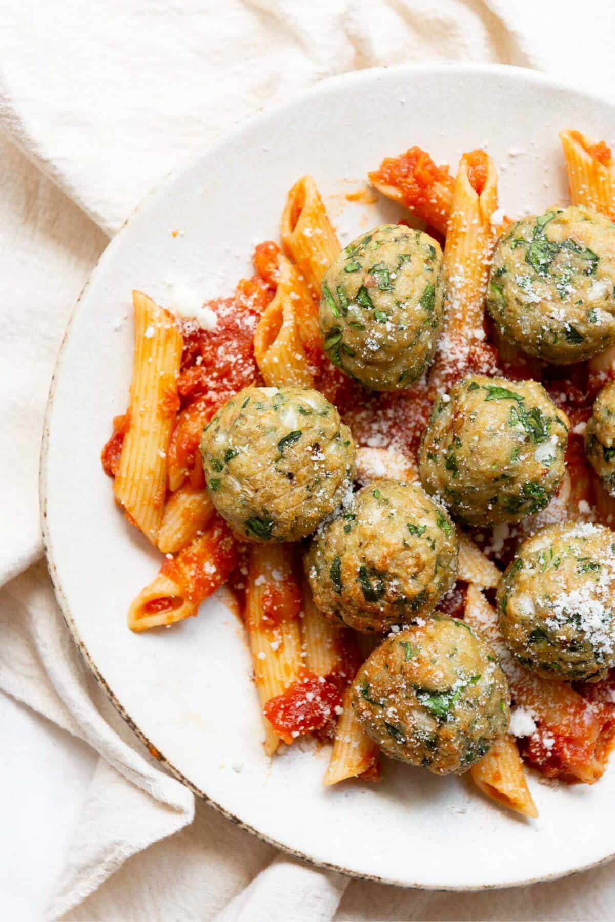 Air fryer chicken meatballs served on a plate with penne pasta and marinara sauce, garnished with fresh parmesan cheese.