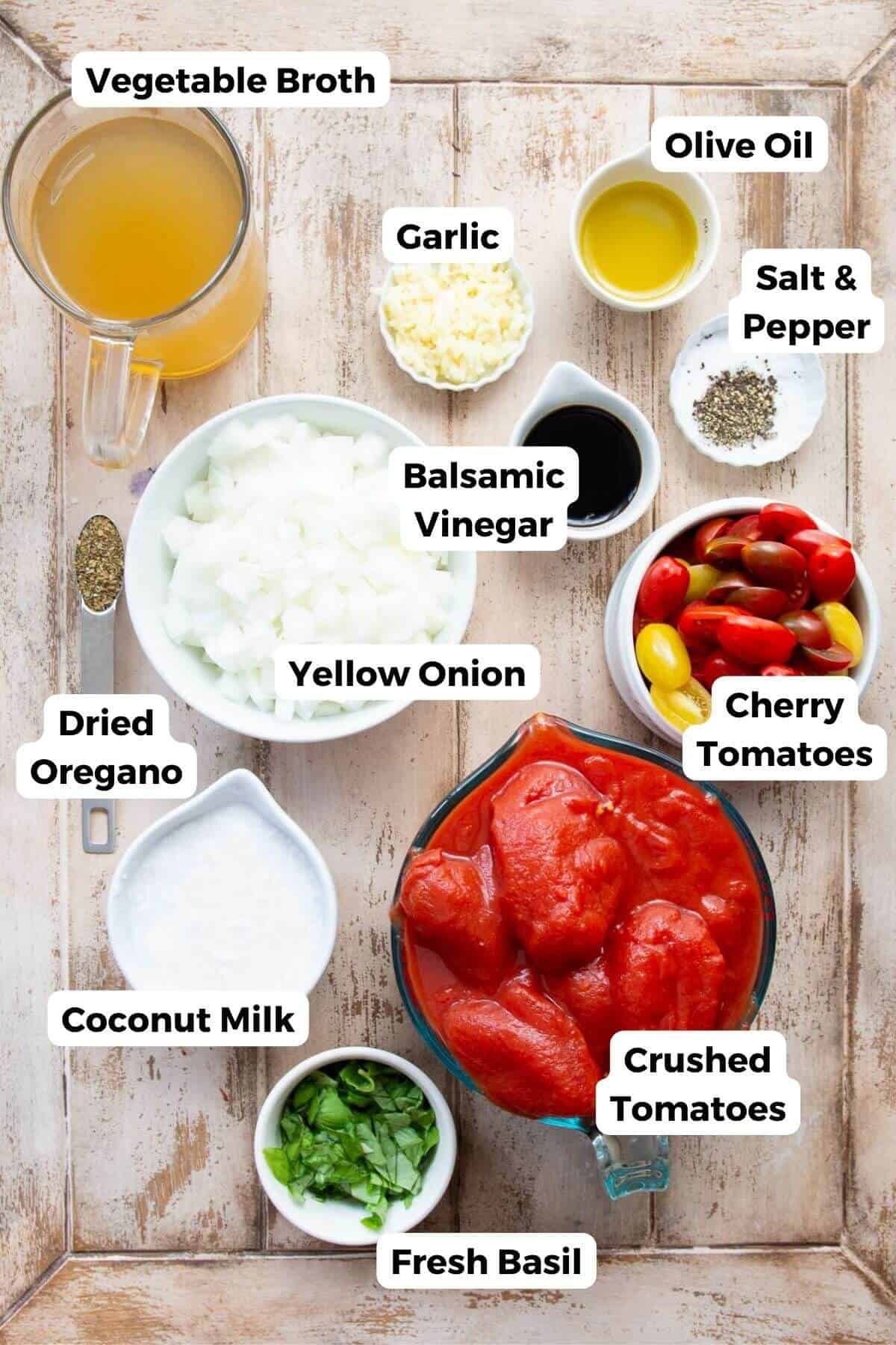 all ingredients in dairy-free tomato soup in small bowls including cherry tomatoes, crushed tomatoes, coconut milk, basil, oregano, balsamic vinegar, salt, fresh garlic, vegetable brother, and olive oil