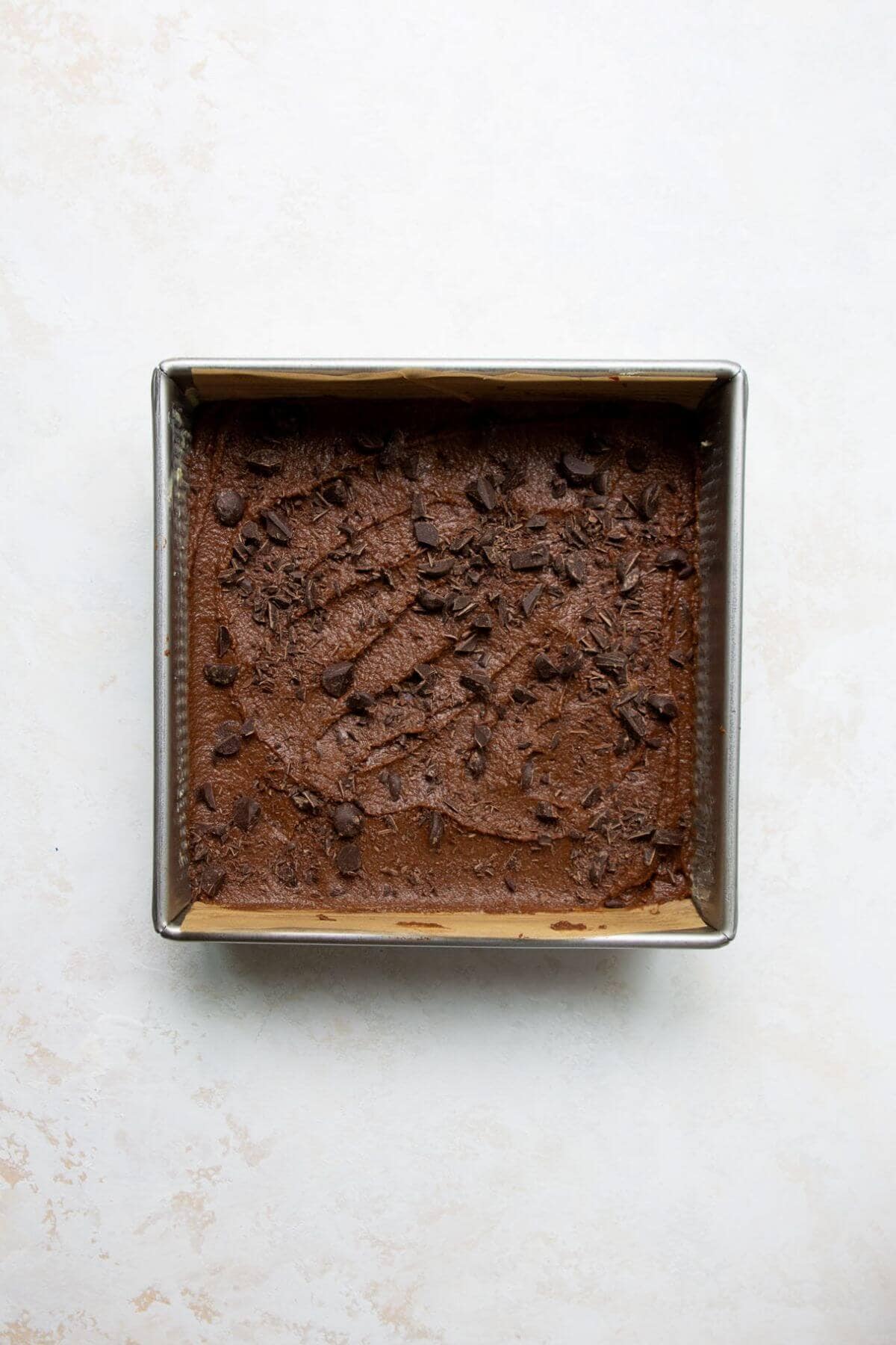 Chickpea brownie batter spread in a parchment lined 8x8 baking pan.
