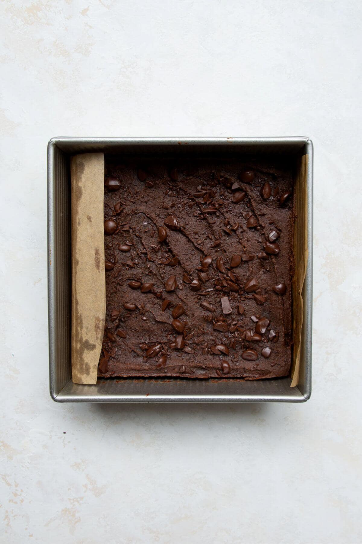 Baked chickpea brownies in a square pan topped with melted chocolate chips.