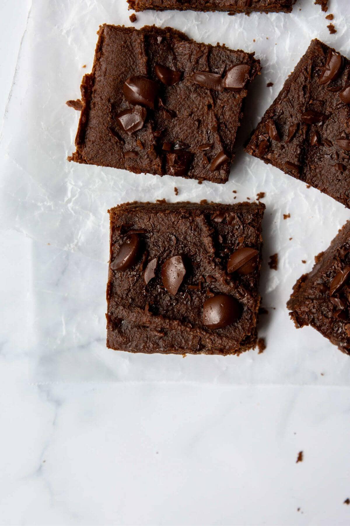 Sliced fudgy chickpea brownies on parchment paper topped with chocolate chunks.