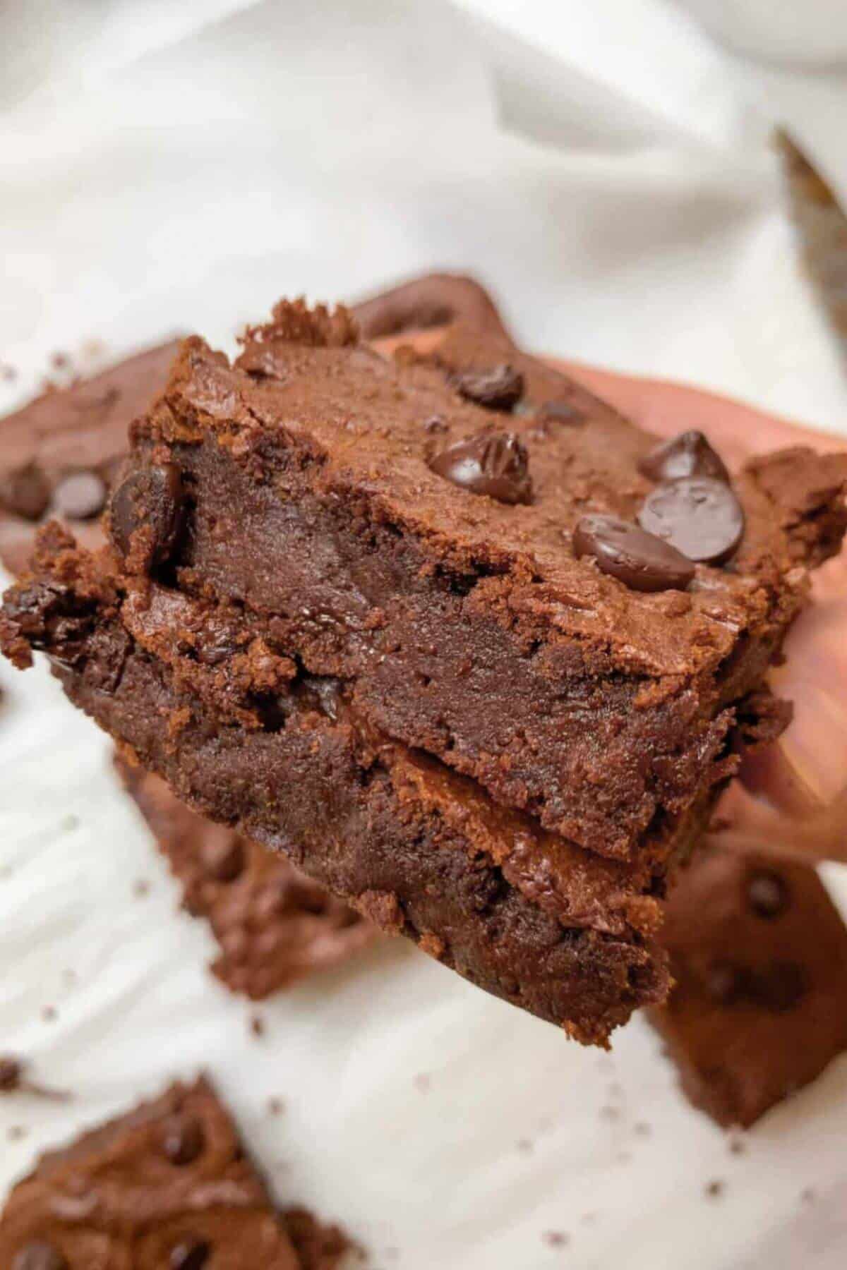 Stack of fudgy chickpea brownies with melted chocolate chunks on top.
