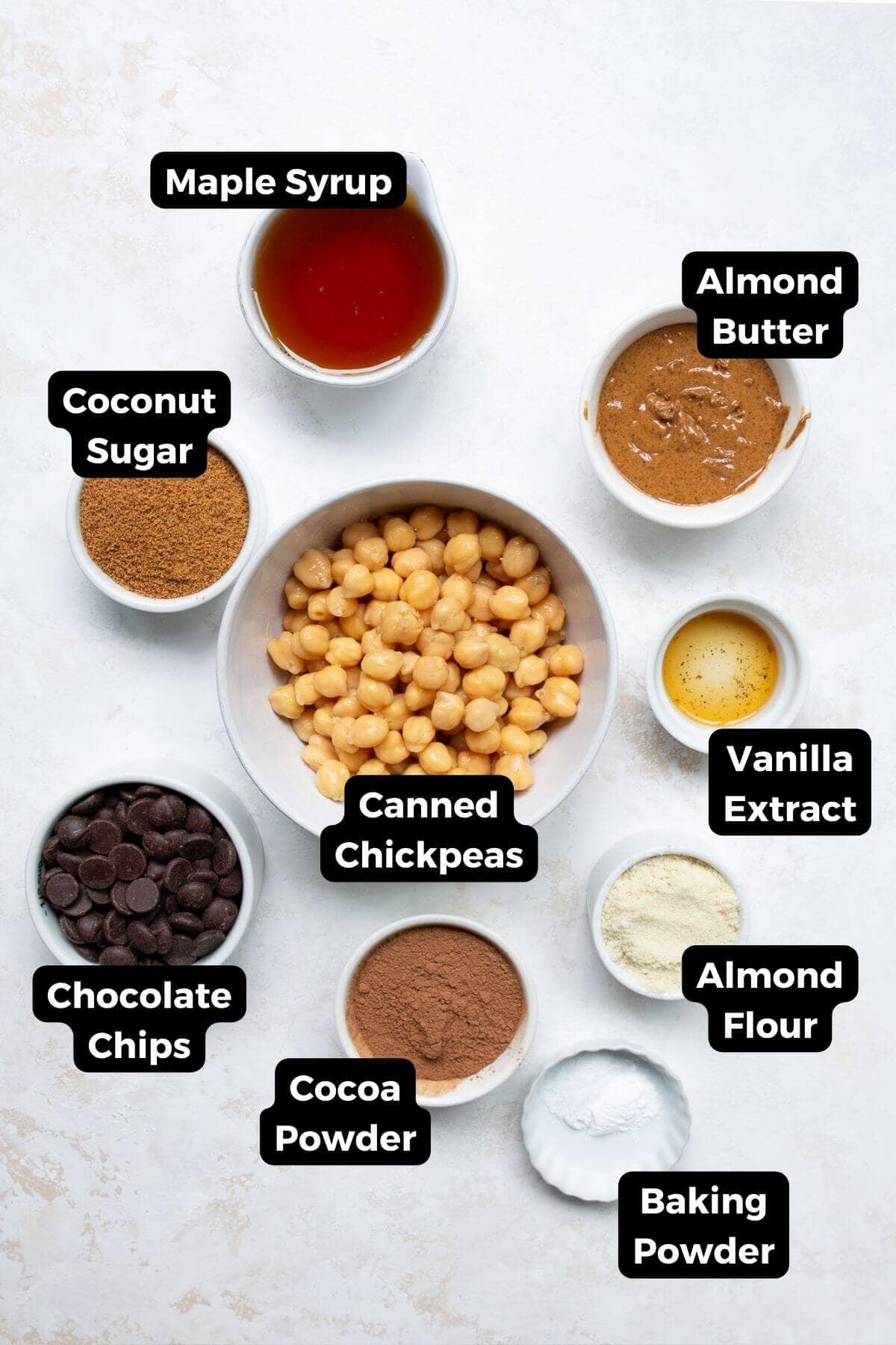 Ingredients for chickpea brownies including canned chickpeas, almond butter, maple syrup, cocoa powder, and almond flour.
