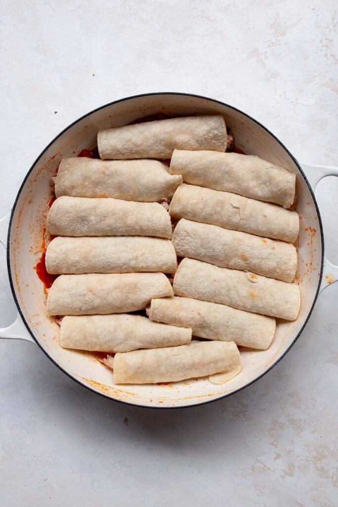 chicken and beans filling rolled up inside corn tortillas in a pan