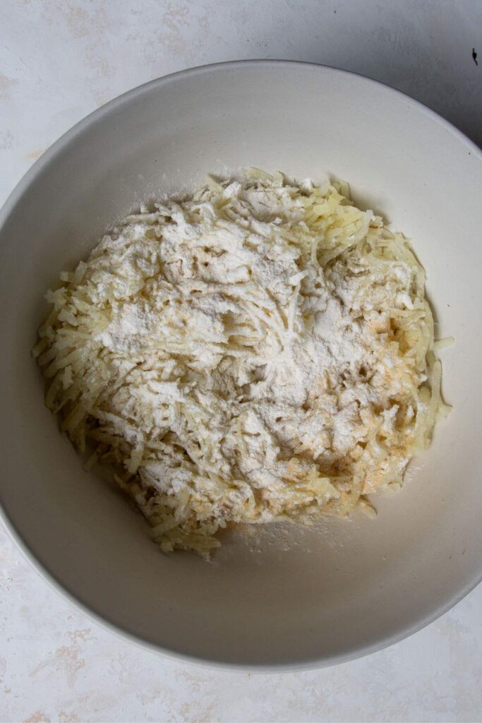 shredded potatoes with gluten-free flour, salt, garlic, and onion powder in a mixing bowl