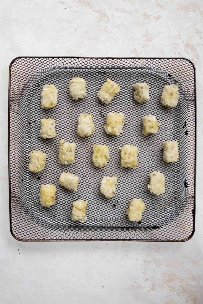uncooked gluten free tater tots in an air fryer basket before cooking