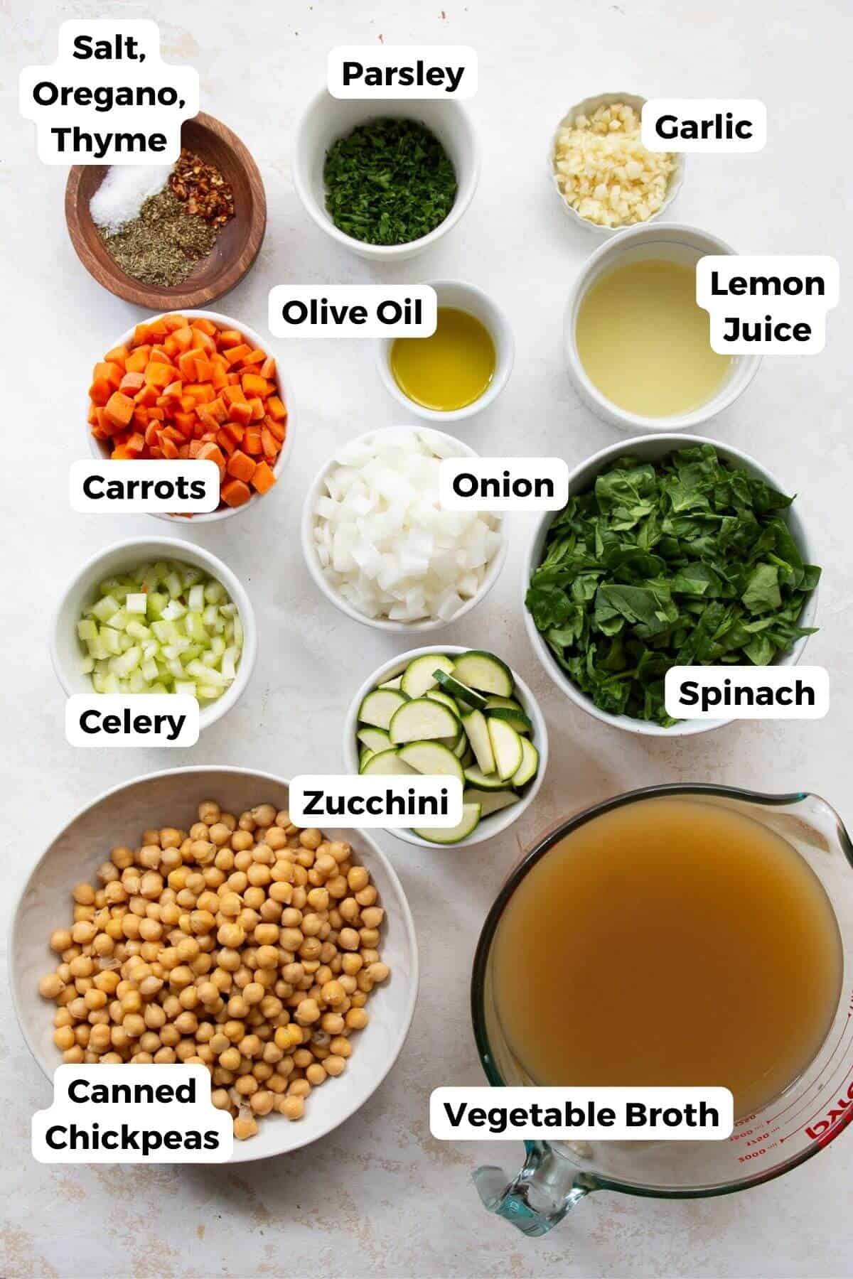 Ingredients for Greek chickpea soup including canned chickpeas, zucchini, carrots, celery, onion, garlic, spinach, lemon, and vegetable broth.