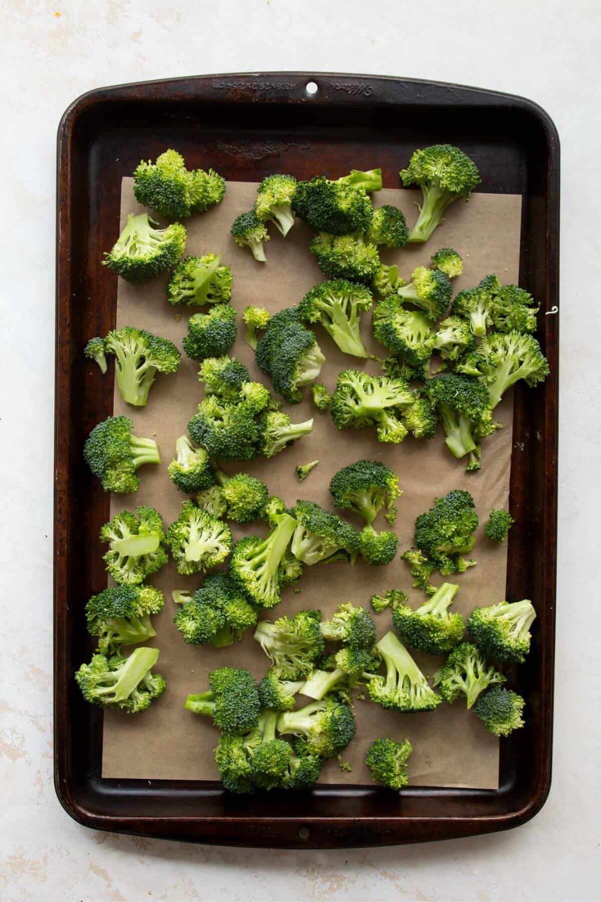 Broccoli florets tossing in olive oil on a baking sheet before roasting in oven.