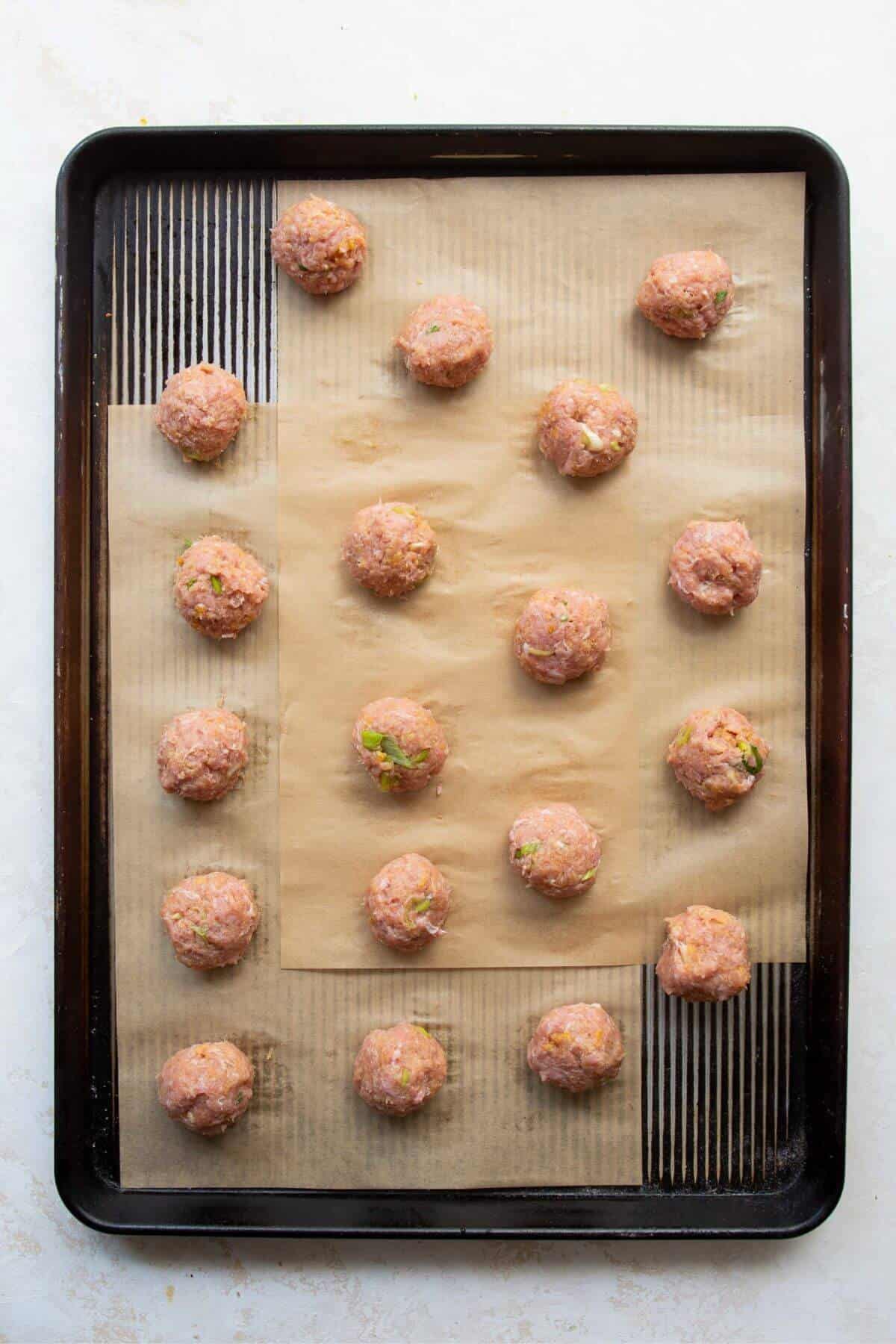 Raw gluten-free Asian turkey meatballs in a baking sheet before baking.