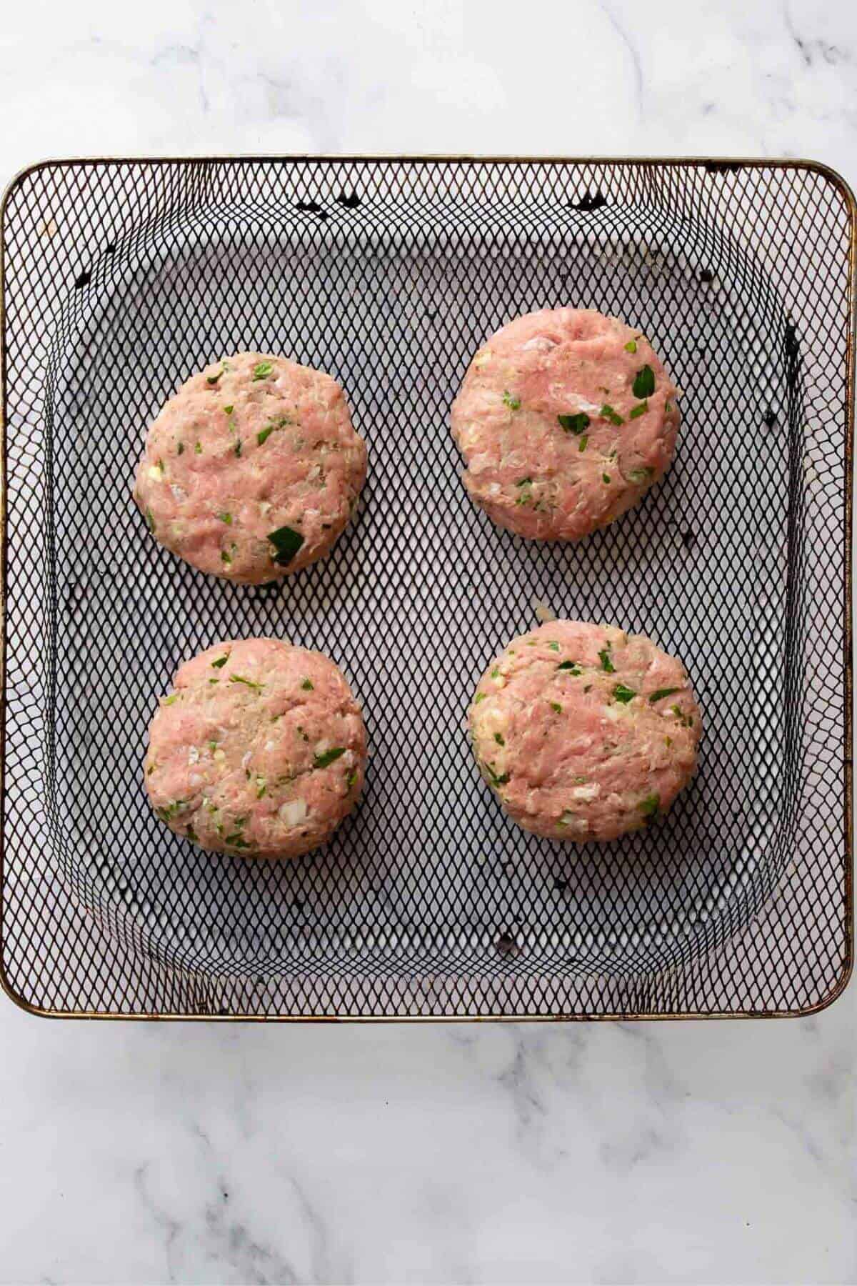 Four raw turkey burgers on an air fryer basket.