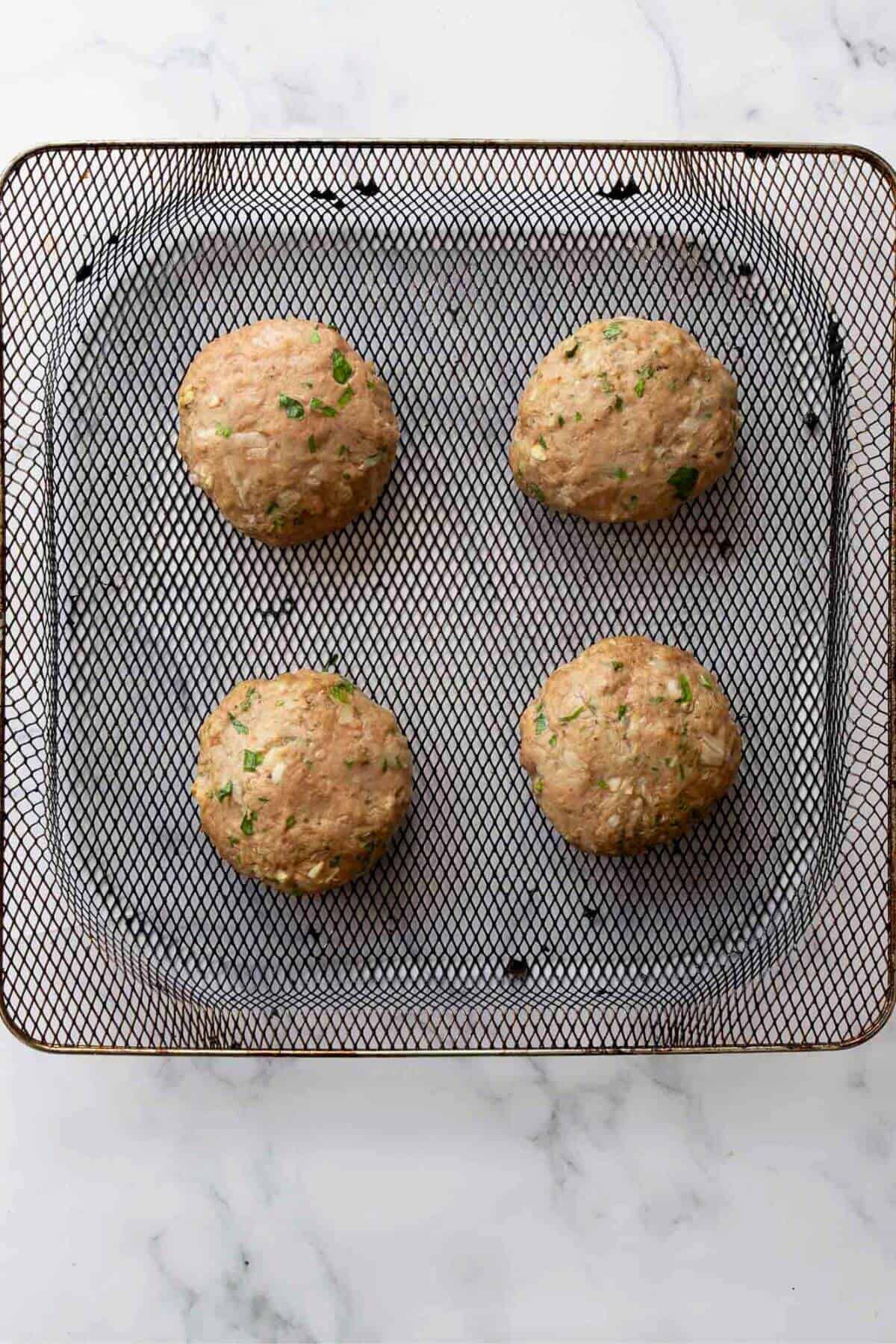 Four cooked and golden turkey burgers on an air fryer basket.