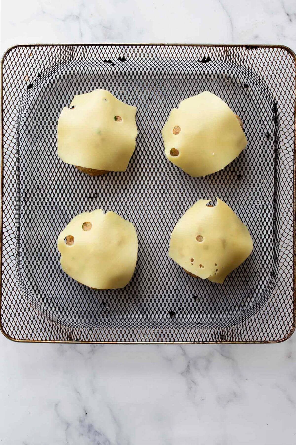 Slices of cheese on top of cooked turkey burgers in air fryer basket.