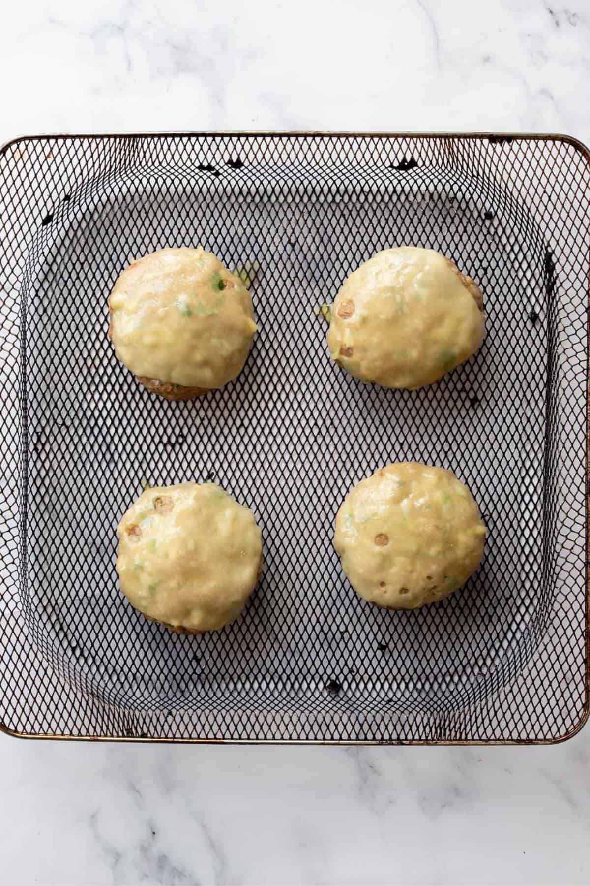 Melted cheese on top of turkey burgers in air fryer basket.