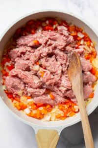 raw ground turkey in a skillet with cooked onions and peppers