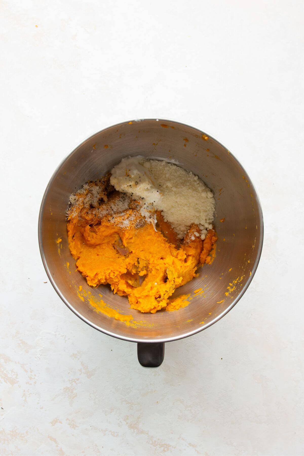 Mashed sweet potatoes in a large bowl with Greek yogurt, Parmesan, and seasonings.
