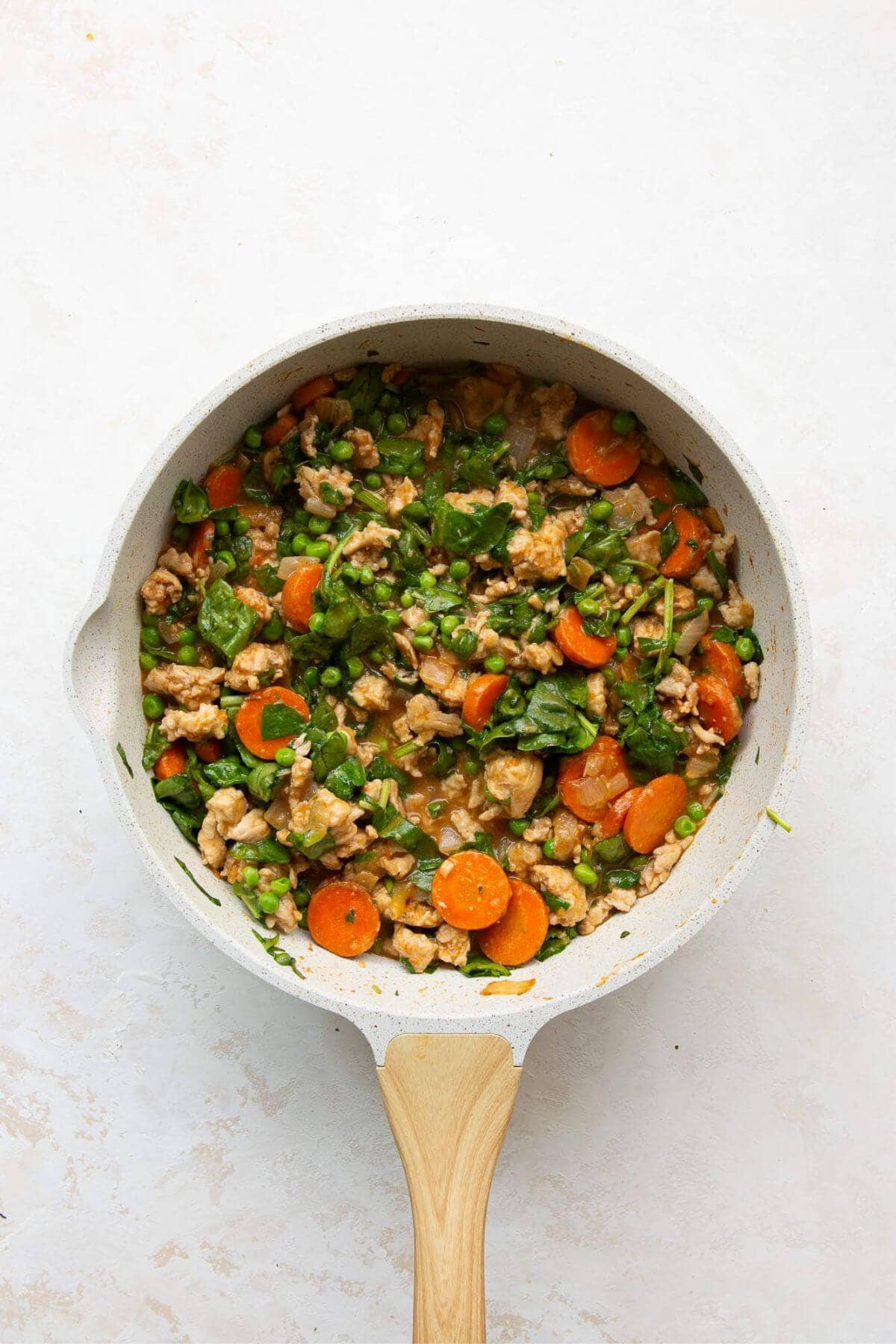Adding chicken broth, peas, and spinach to the skillet and simmering until the sauce thickens.