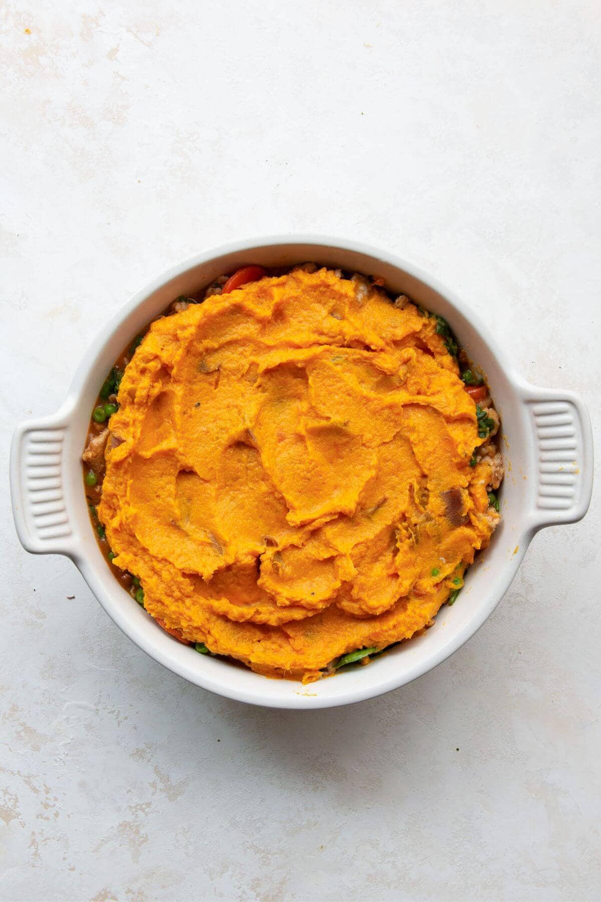 Topping the filling with mashed sweet potatoes and smoothing the surface with a spatula.