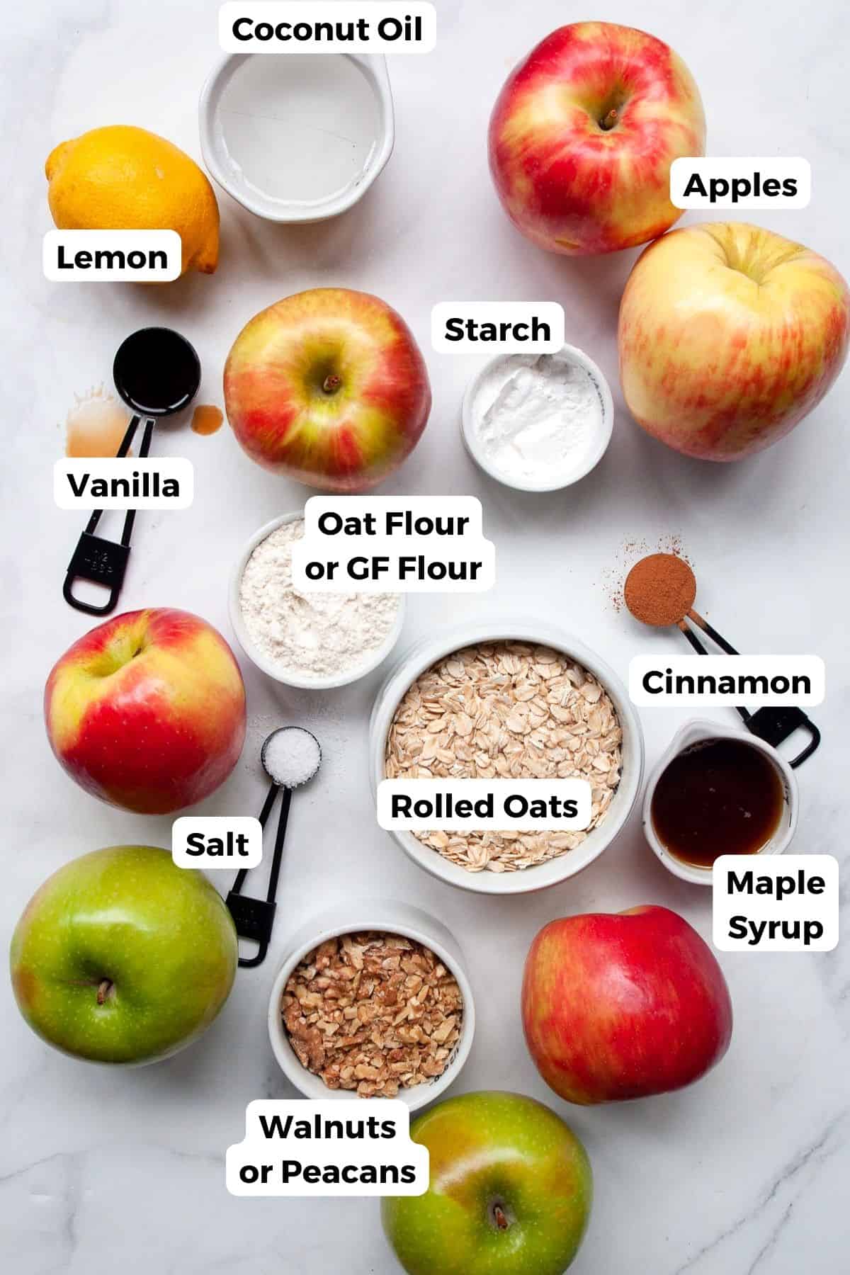 All the ingredients for healthy apple crisp in small bowls with labels, including sliced apples, rolled oats, maple syrup, coconut oil, walnuts, cinnamon, lemon, and tapioca flour.