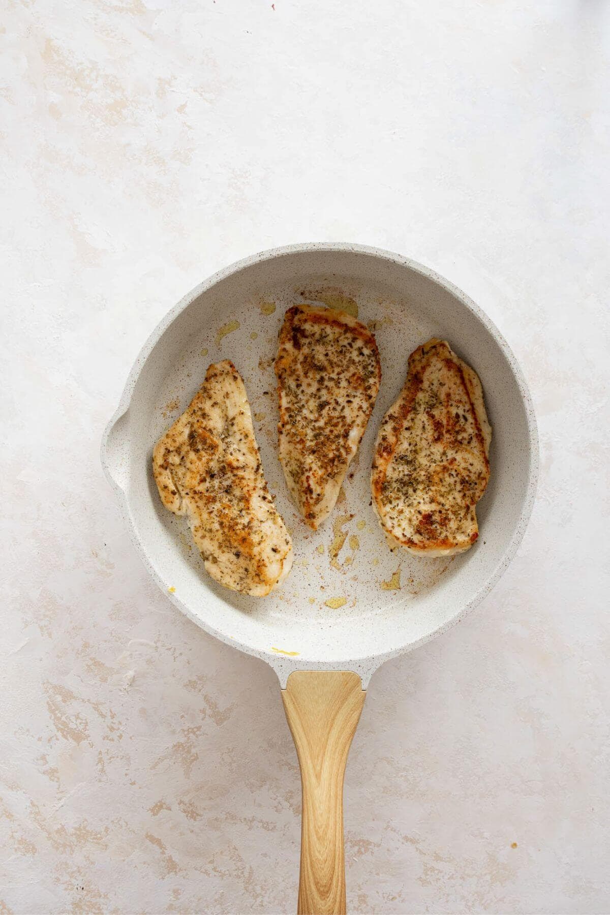 Seasoned chicken breasts searing in a skillet for penne alla vodka.